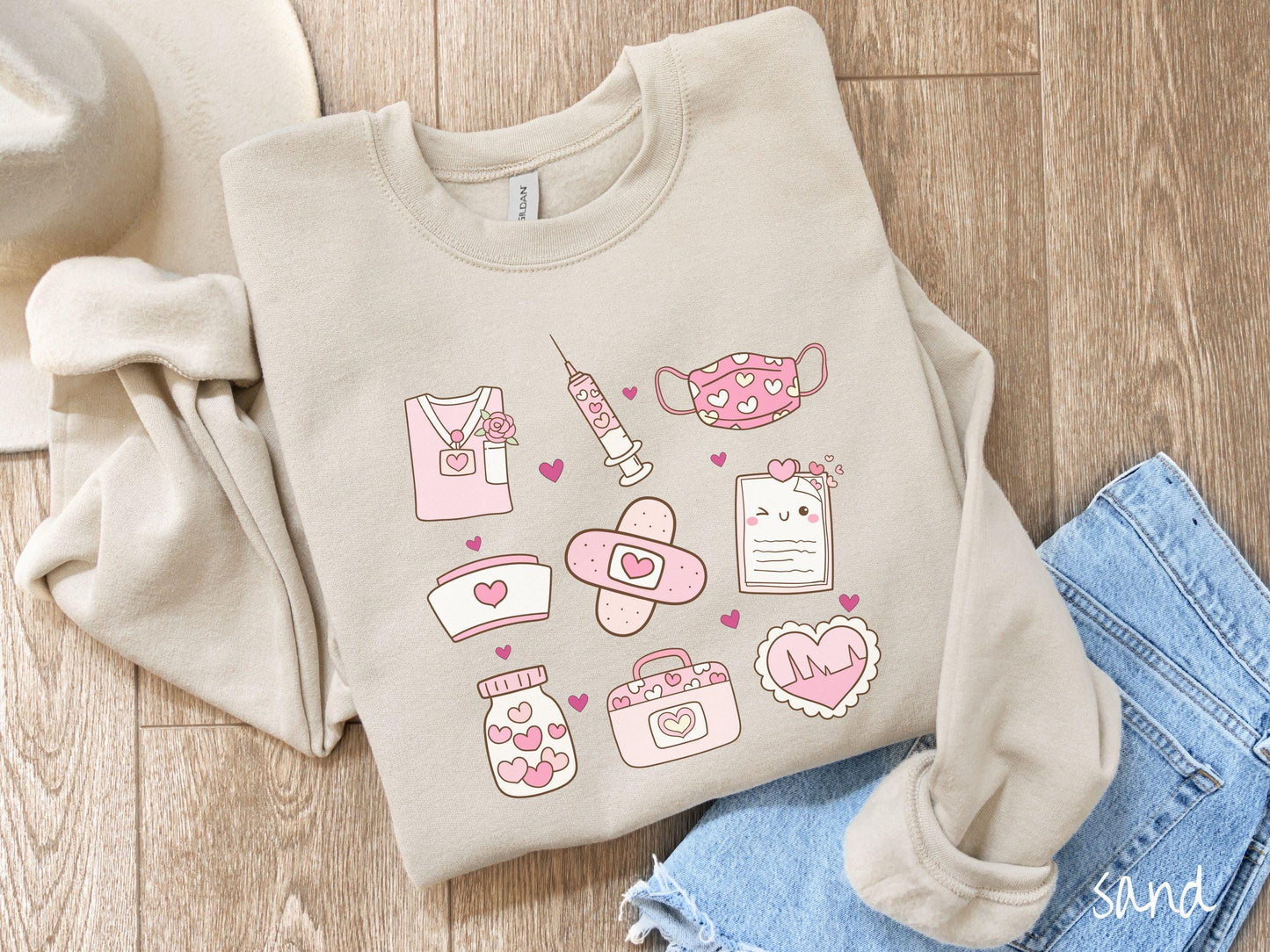 A Gildan sweatshirt featuring a 3x3 grid of nursing-themed illustrations adorned with heart designs like nursing scrubs, syringes, a face mask, a nurse cap, bandages, medical records, vitamins, a medical bag, and a heart-shaped EKG graph.