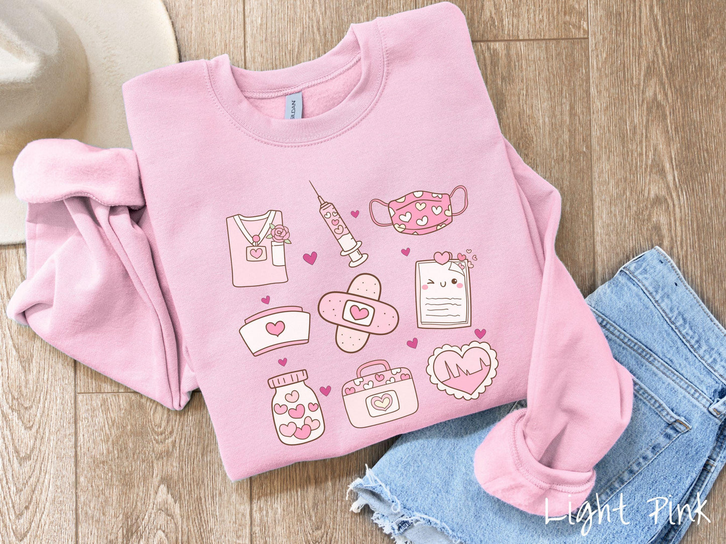 A Gildan sweatshirt featuring a 3x3 grid of nursing-themed illustrations adorned with heart designs like nursing scrubs, syringes, a face mask, a nurse cap, bandages, medical records, vitamins, a medical bag, and a heart-shaped EKG graph.
