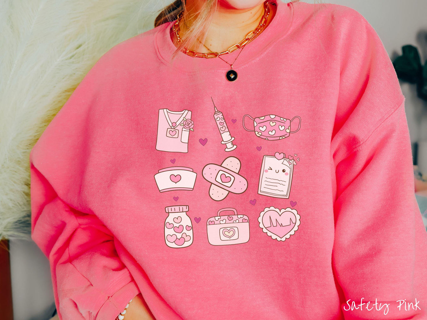 A Gildan sweatshirt featuring a 3x3 grid of nursing-themed illustrations adorned with heart designs like nursing scrubs, syringes, a face mask, a nurse cap, bandages, medical records, vitamins, a medical bag, and a heart-shaped EKG graph.