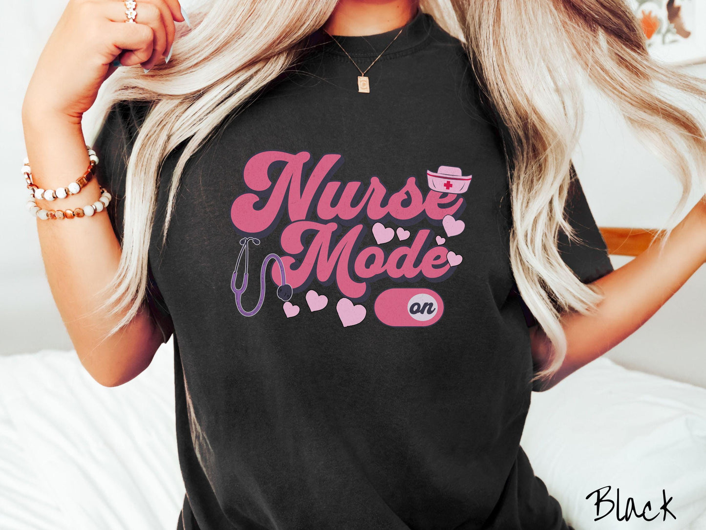 A stylish Comfort Colors t-shirt design features the text "Nurse Mode" in bold pink font with a pink nurse's cap placed over the letter E, and a stethoscope positioned beneath the text, alongside an "on" button widget set to the on position.