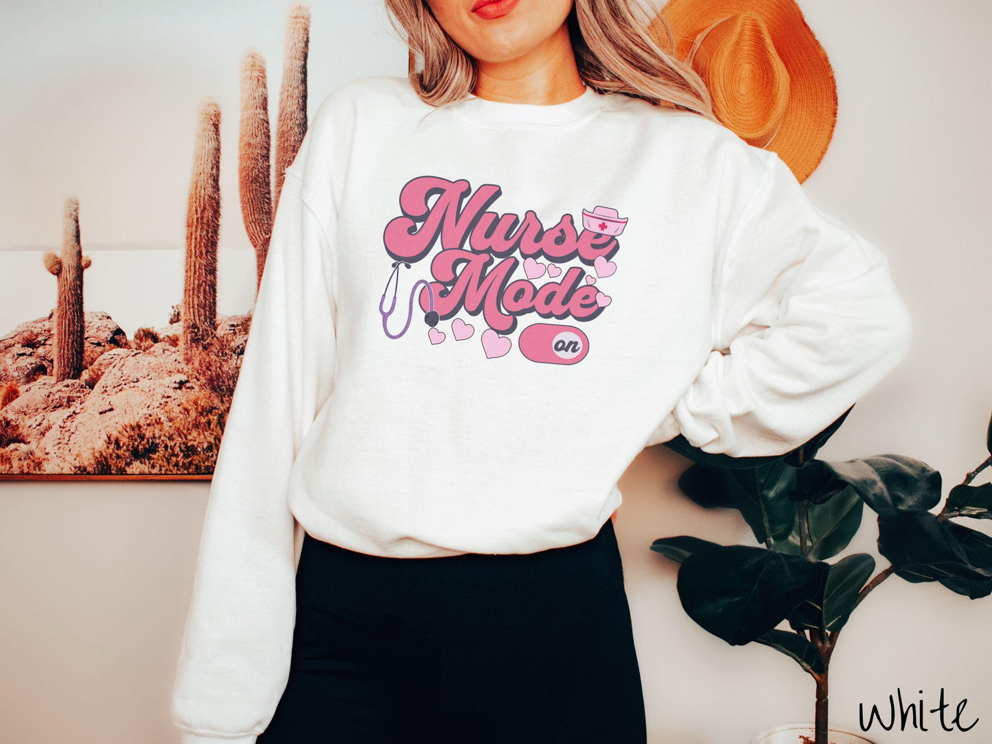 A stylish Gildan sweatshirt design features the text "Nurse Mode" in bold pink font with a pink nurse's cap placed over the letter E, and a stethoscope positioned beneath the text, alongside an "on" button widget set to the on position.