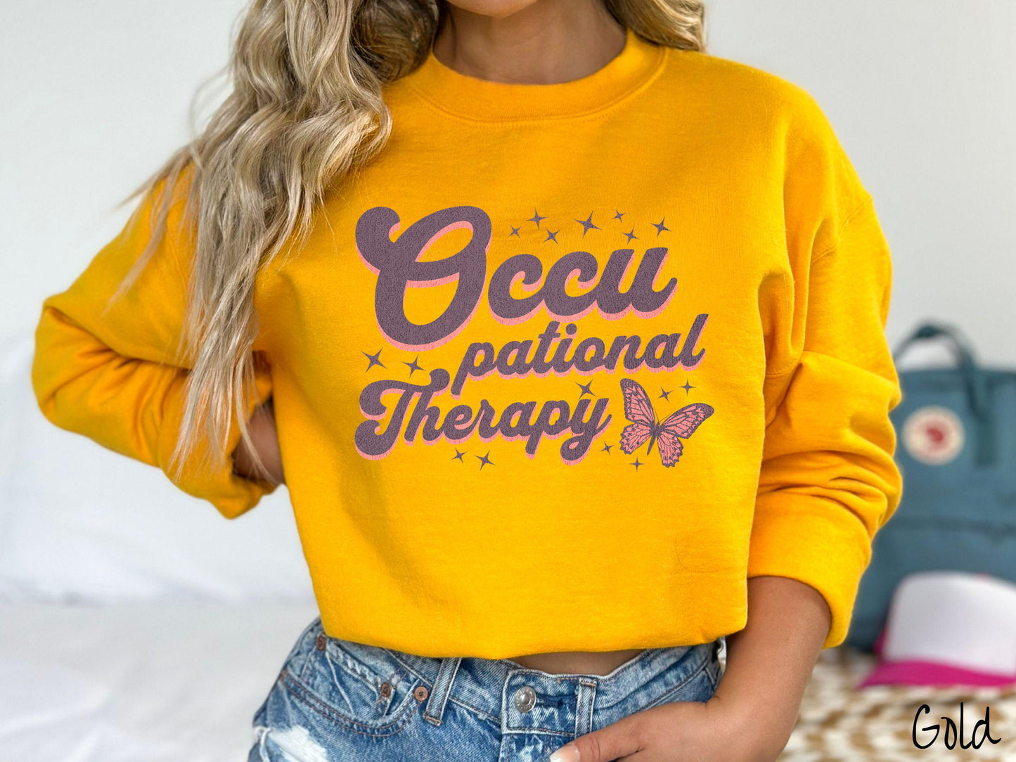 A vintage, gold colored Gildan sweatshirt featuring the words Occupational Therapy across the front, this unique design showcases a stunning pink and dark purple butterfly surrounded by delicate twinkling stars.