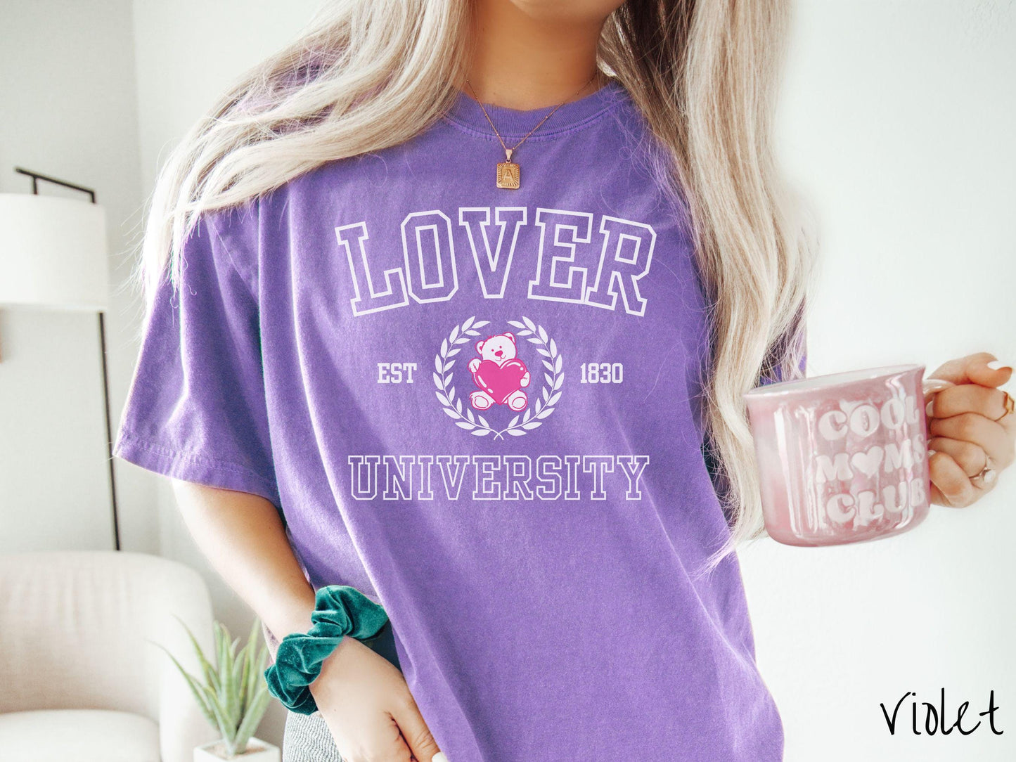 A vintage Comfort Colors t-shirt featuring a university logo-inspired design showcasing the text “Lover University” in collegiate-style font. Two pink laurel leaves frame a pink teddy bear hugging a heart with the text “EST. 1830” in pink font.
