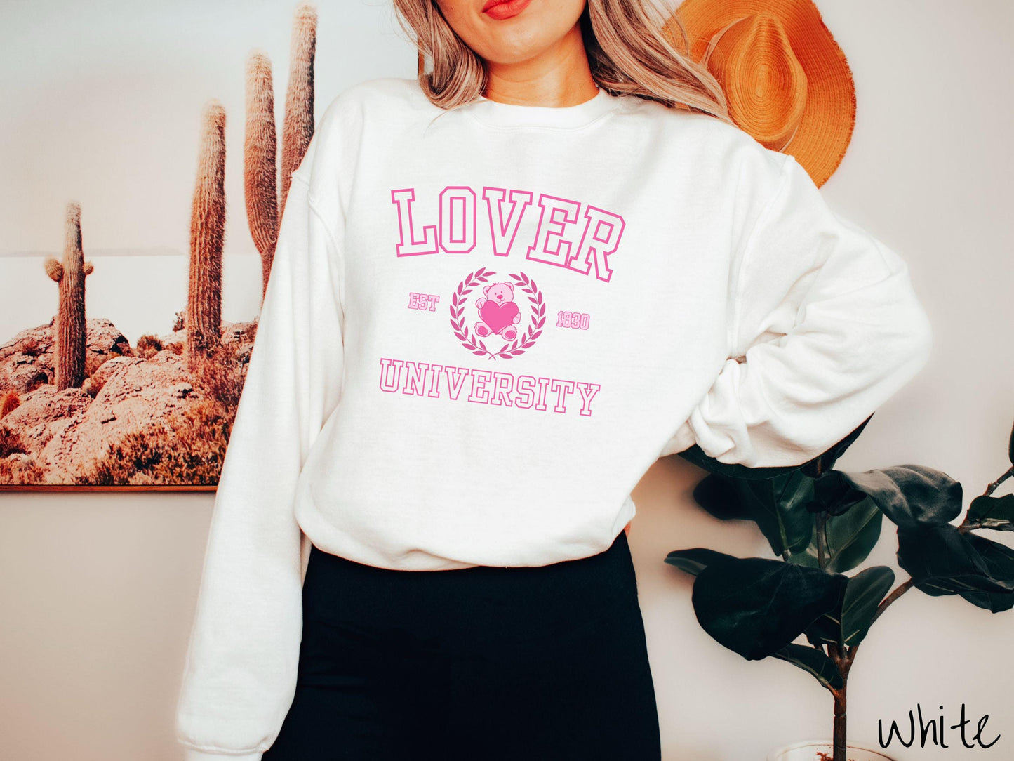 A vintage Gildan sweatshirt featuring a university logo-inspired design showcasing the text “Lover University” in collegiate-style font. Two pink laurel leaves frame a pink teddy bear hugging a heart with the text “EST. 1830” in pink font.