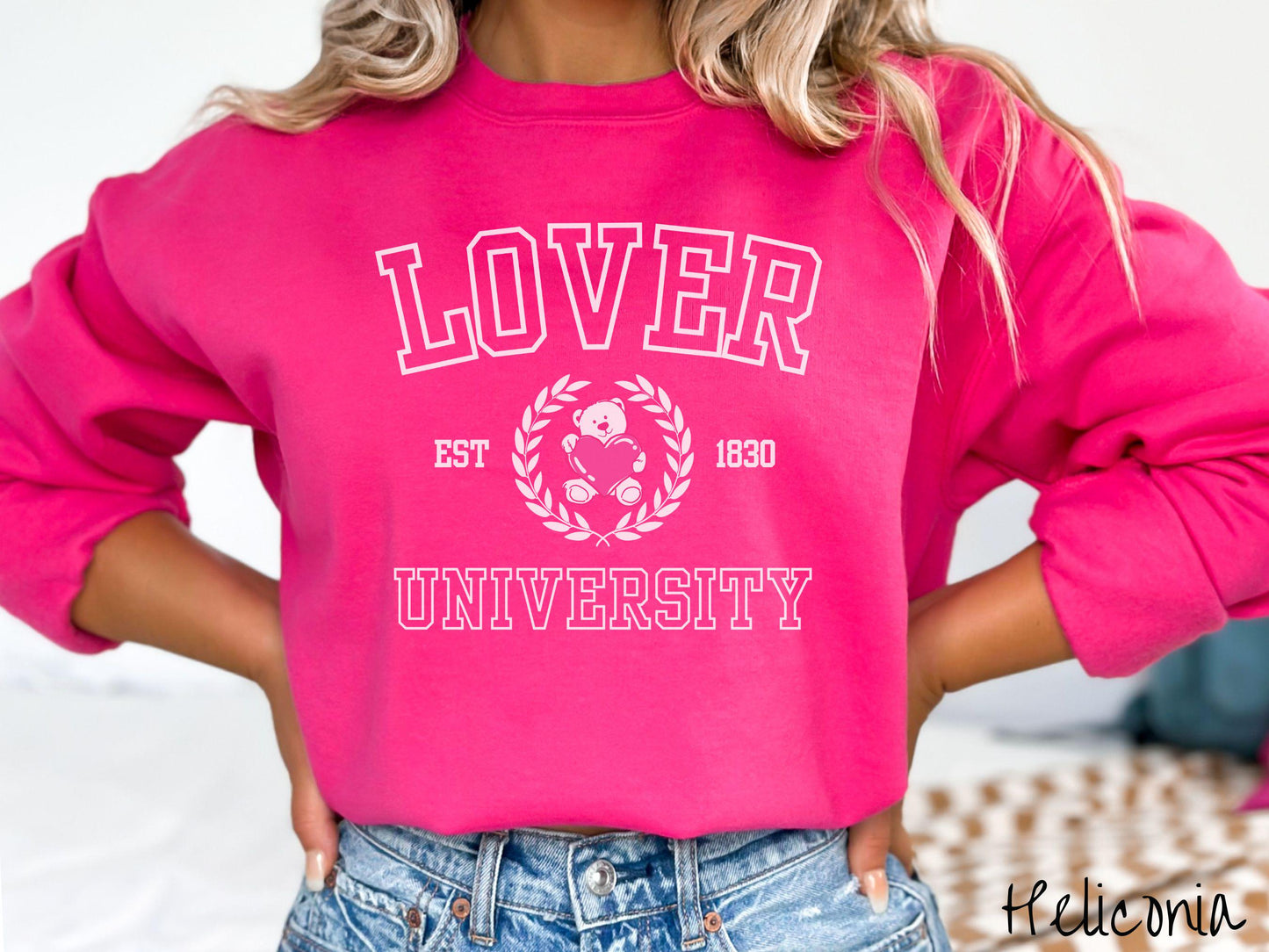 A vintage Gildan sweatshirt featuring a university logo-inspired design showcasing the text “Lover University” in collegiate-style font. Two pink laurel leaves frame a pink teddy bear hugging a heart with the text “EST. 1830” in pink font.