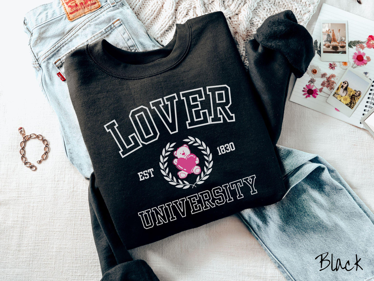 A vintage Gildan sweatshirt featuring a university logo-inspired design showcasing the text “Lover University” in collegiate-style font. Two pink laurel leaves frame a pink teddy bear hugging a heart with the text “EST. 1830” in pink font.