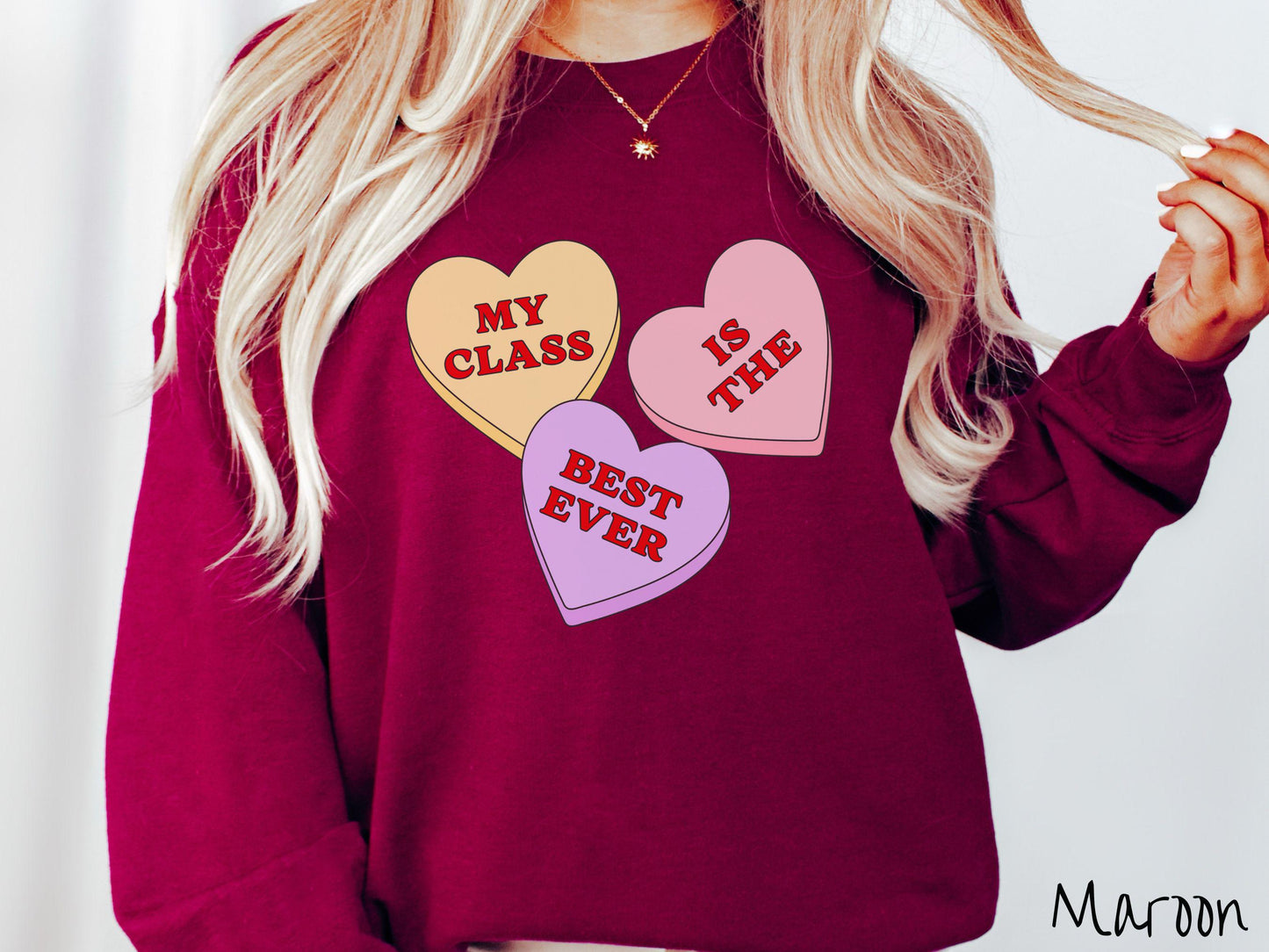 A charming vintage-style Valentine’s Day Gildan sweatshirt featuring three vibrant conversation hearts in yellow, red, and purple, this design displays the text “My class is the best ever” spread across the hearts.