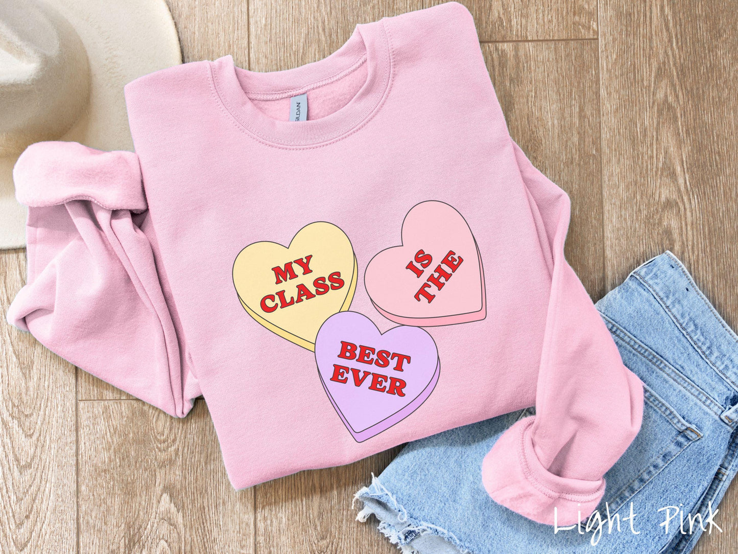 A charming vintage-style Valentine’s Day Gildan sweatshirt featuring three vibrant conversation hearts in yellow, red, and purple, this design displays the text “My class is the best ever” spread across the hearts.