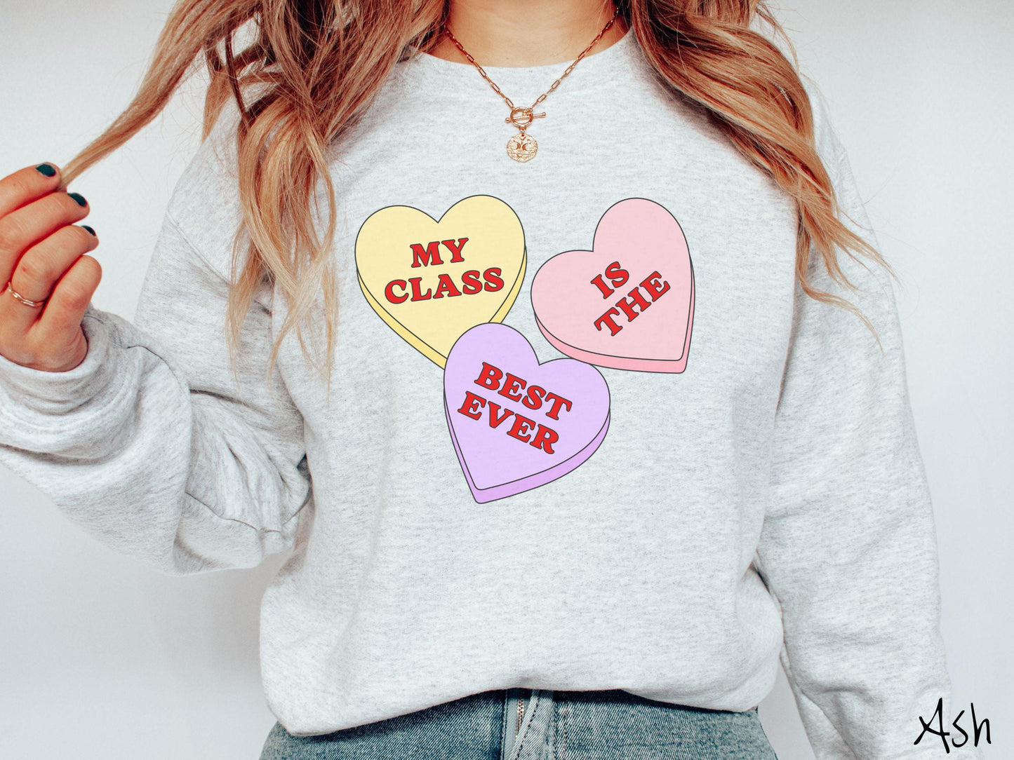 A charming vintage-style Valentine’s Day Gildan sweatshirt featuring three vibrant conversation hearts in yellow, red, and purple, this design displays the text “My class is the best ever” spread across the hearts.
