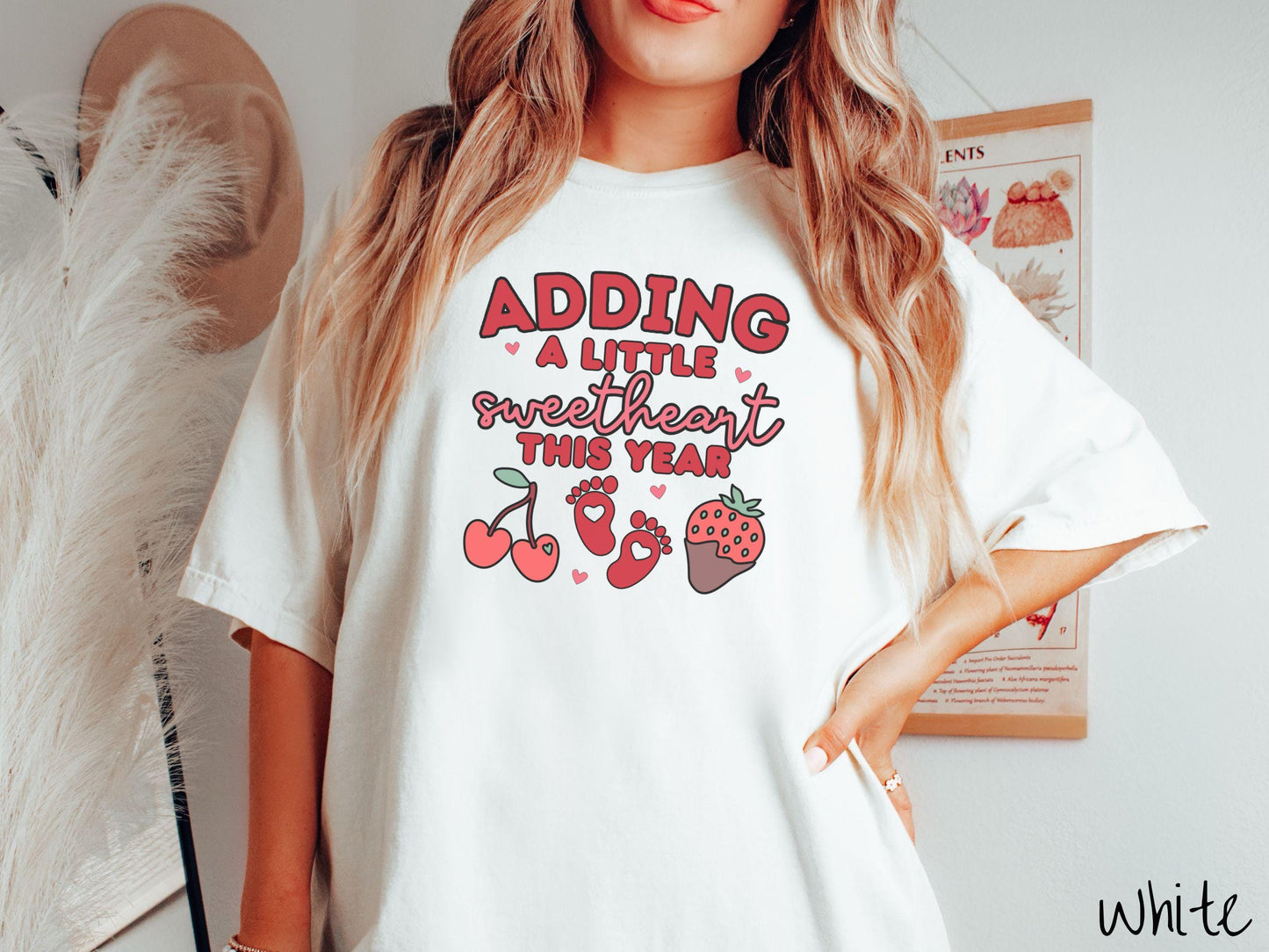 Share your exciting news with this vintage Comfort Colors t-shirt featuring the phrase “Adding a little sweetheart this year” in bold red font, paired with two red baby footprints framed by two red cherries and a chocolate-covered strawberry.