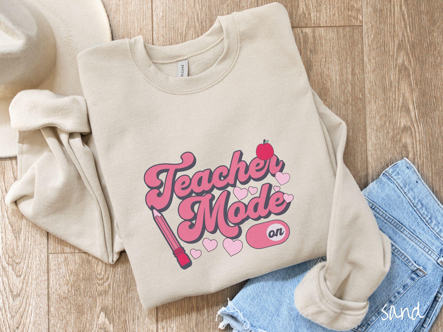 A vintage Gildan sweathirt featuring the phrase “Teacher Mode” in playful pink font, an “On” button toggled to the “On” position, and with charming details like a red pencil, a red apple, and pink hearts sprinkled throughout.