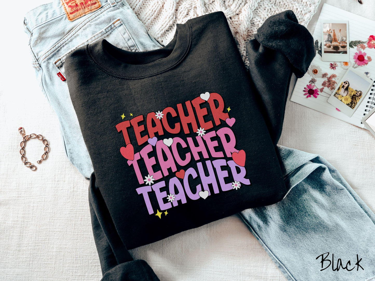 A vibrant vintage Gildan sweatshirt featuring the word “Teacher” written vertically three times in bold red, pink, and purple font, with colorful hearts, flowers, and twinkling stars scattered throughout for a whimsical and eye-catching look.