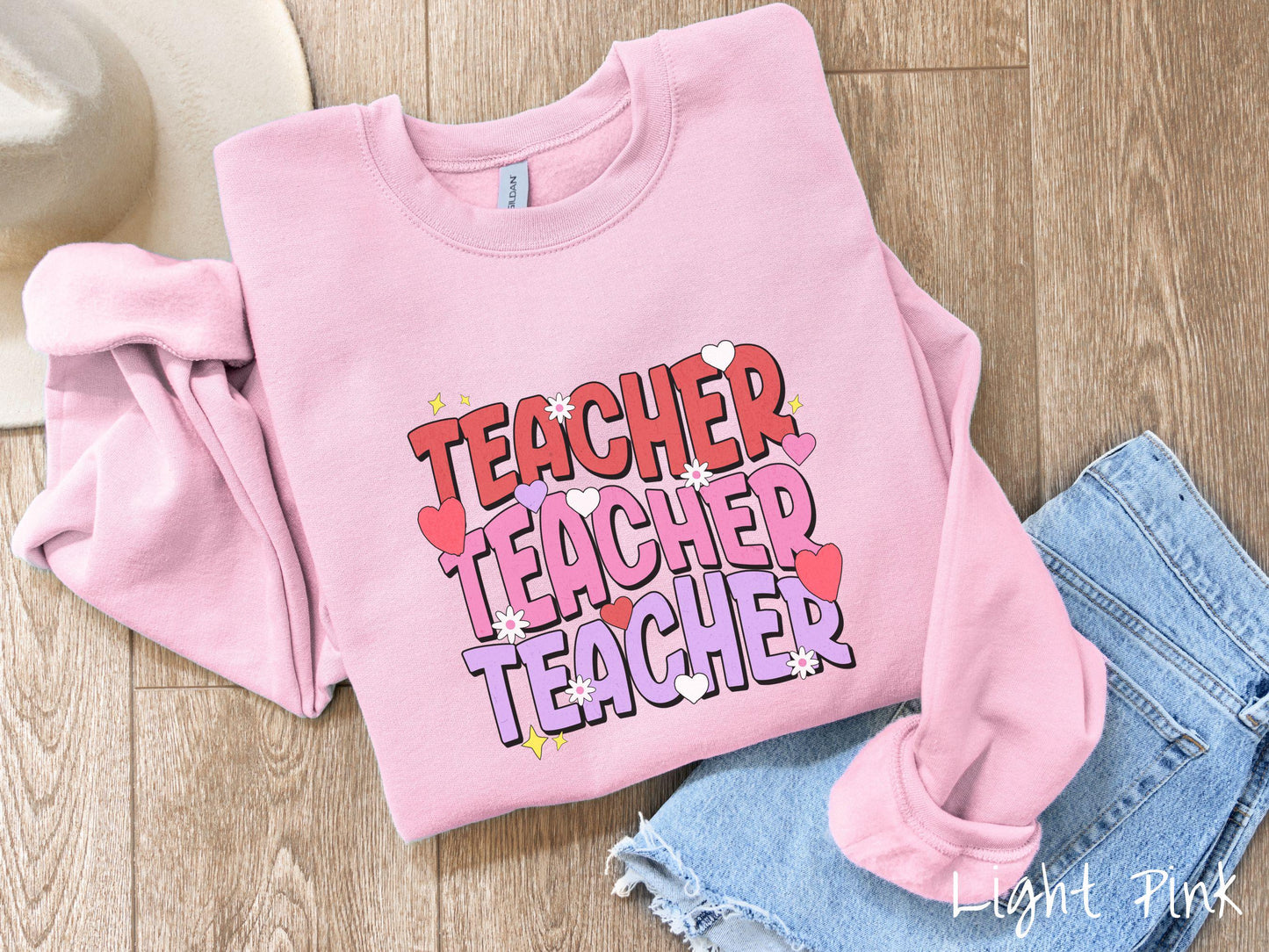 A vibrant vintage Gildan sweatshirt featuring the word “Teacher” written vertically three times in bold red, pink, and purple font, with colorful hearts, flowers, and twinkling stars scattered throughout for a whimsical and eye-catching look.