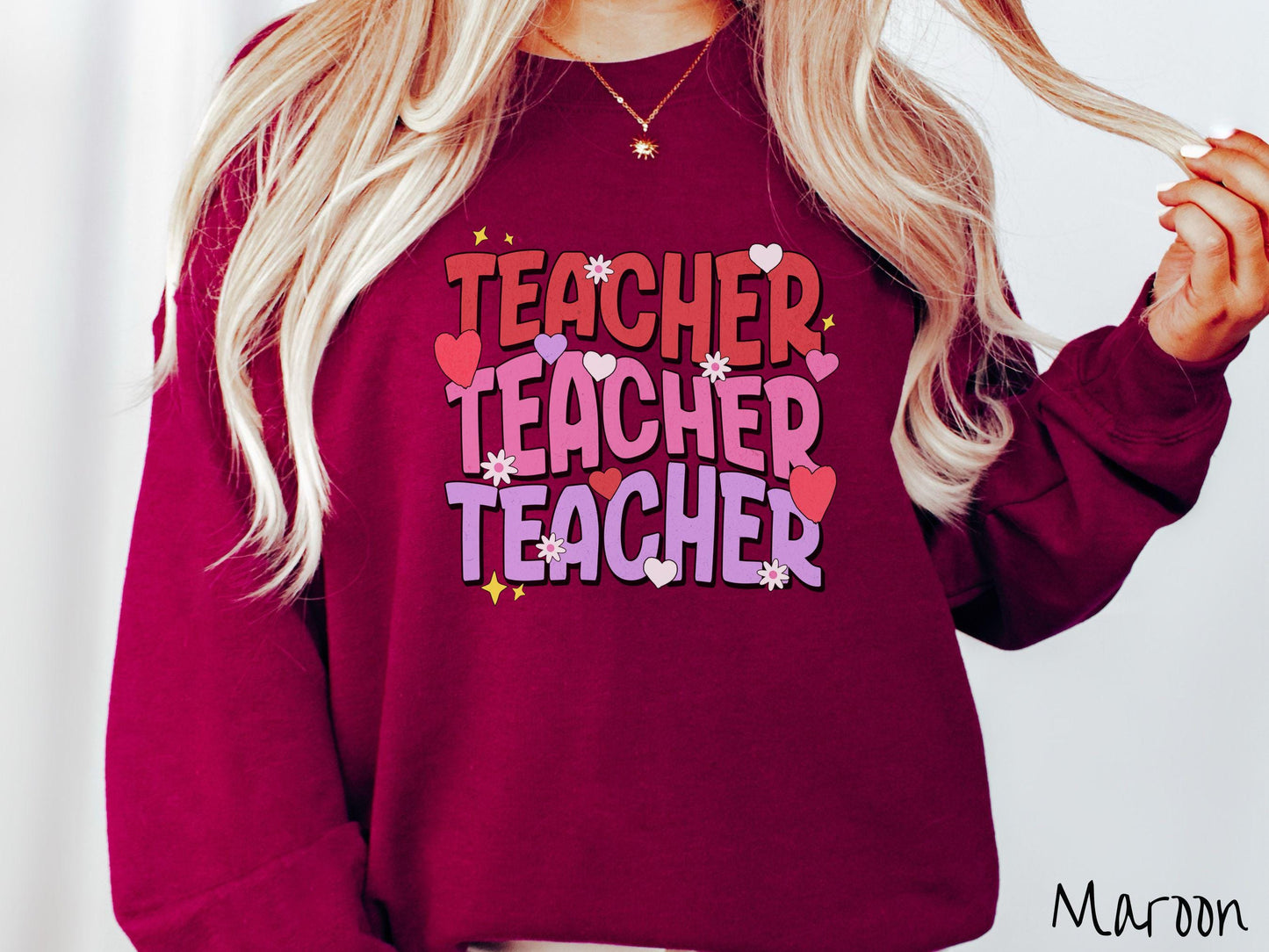 A vibrant vintage Gildan sweatshirt featuring the word “Teacher” written vertically three times in bold red, pink, and purple font, with colorful hearts, flowers, and twinkling stars scattered throughout for a whimsical and eye-catching look.