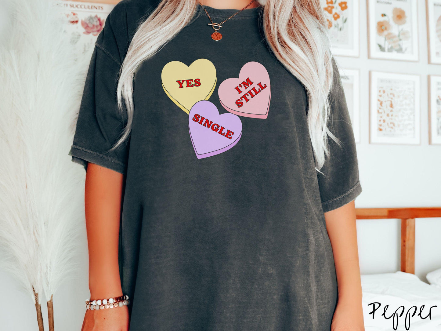 Make a bold statement this Valentine’s Day with this vintage Comfort Colors t-shirt featuring three vibrant conversation hearts in yellow, red, and purple, the design showcasing the cheeky phrase “Yes, I’m Still Single” spread across the hearts.