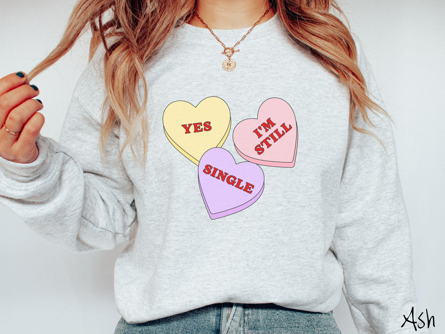 Make a bold statement this Valentine’s Day with this vintage Gildan sweatshirt featuring three vibrant conversation hearts in yellow, red, and purple, the design showcasing the cheeky phrase “Yes, I’m Still Single” spread across the hearts.