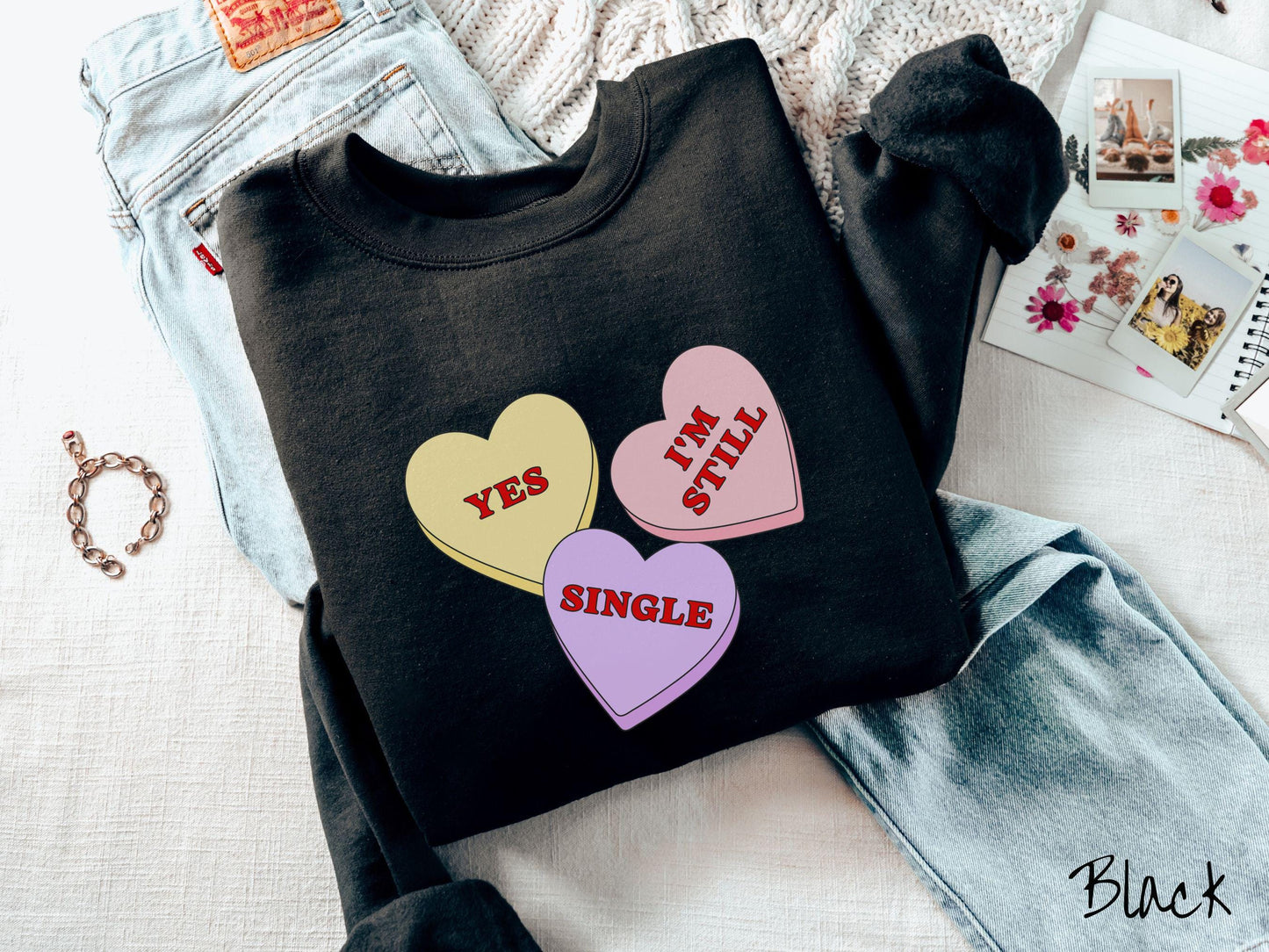 Make a bold statement this Valentine’s Day with this vintage Gildan sweatshirt featuring three vibrant conversation hearts in yellow, red, and purple, the design showcasing the cheeky phrase “Yes, I’m Still Single” spread across the hearts.