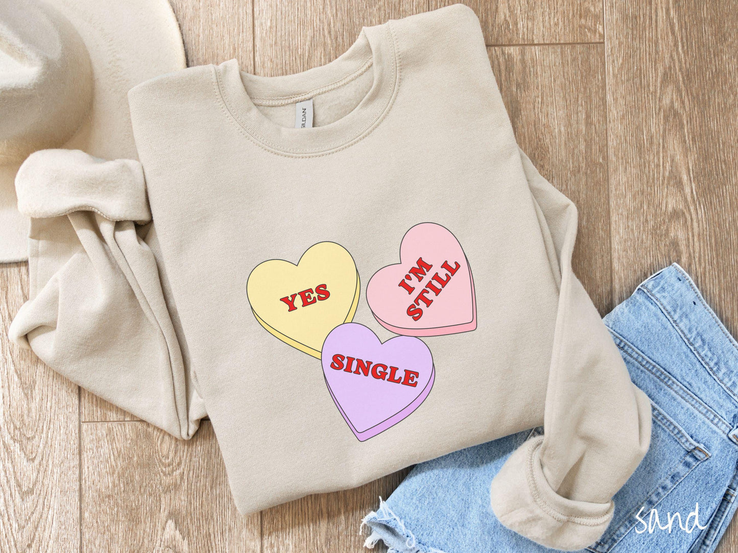Make a bold statement this Valentine’s Day with this vintage Gildan sweatshirt featuring three vibrant conversation hearts in yellow, red, and purple, the design showcasing the cheeky phrase “Yes, I’m Still Single” spread across the hearts.