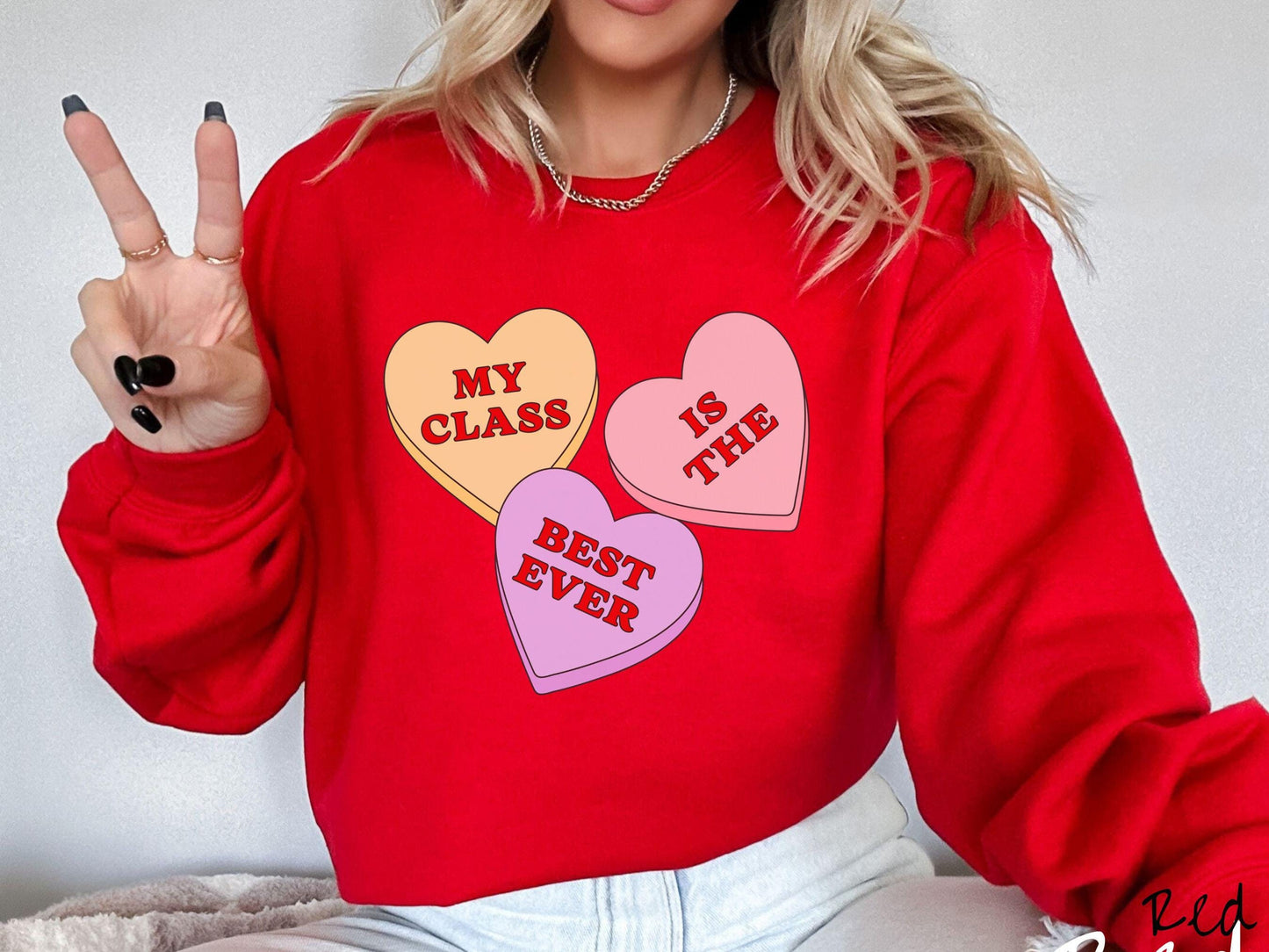 A charming vintage-style Valentine’s Day Gildan sweatshirt featuring three vibrant conversation hearts in yellow, red, and purple, this design displays the text “My class is the best ever” spread across the hearts.