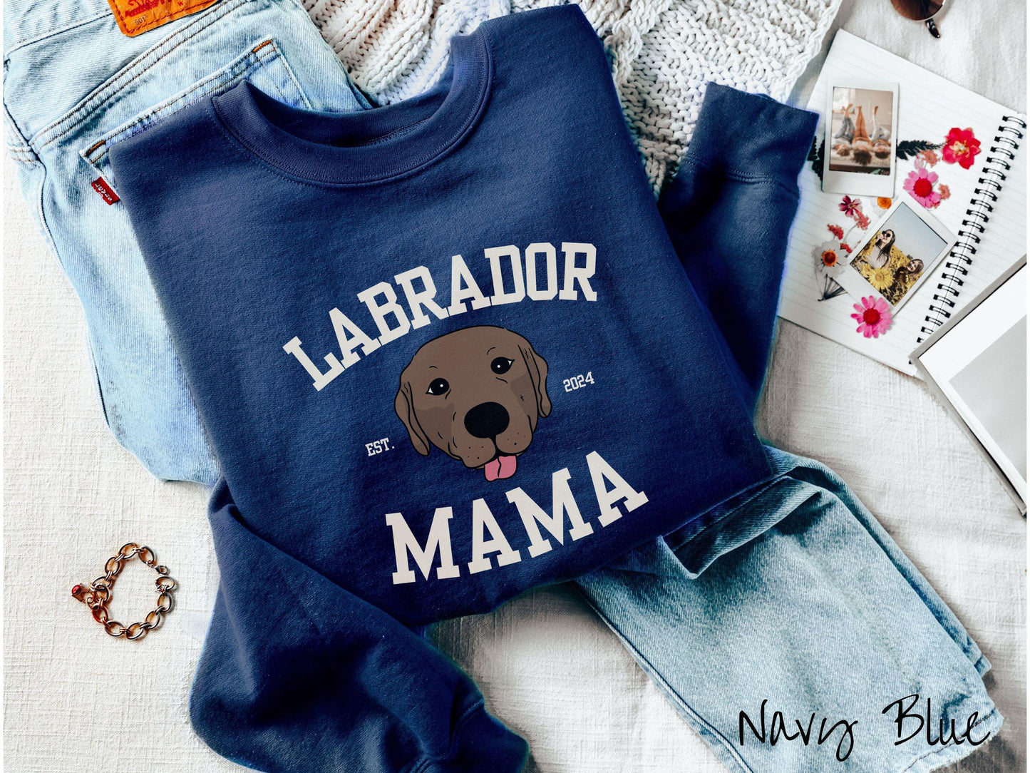 A vintage Gildan sweatshirt featuring bold block lettering that reads 'Labrador Mama.' At the center of the design, a playful chocolate Labrador with its tongue out steals the spotlight, framed by the stylish text 'EST. 2024.'