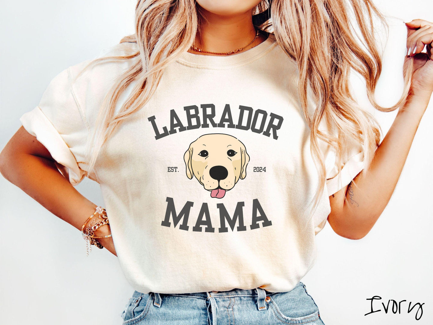 A vintage Comfort Colors t-shirt featuring bold block lettering that reads 'Labrador Mama.' At the center of the design, a playful yellow Labrador with its tongue out steals the spotlight, framed by the stylish text 'EST. 2024.'