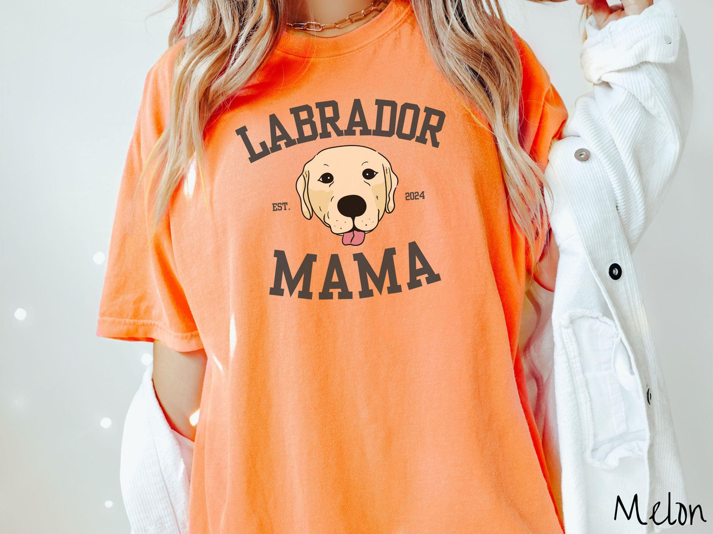 A vintage Comfort Colors t-shirt featuring bold block lettering that reads 'Labrador Mama.' At the center of the design, a playful yellow Labrador with its tongue out steals the spotlight, framed by the stylish text 'EST. 2024.'