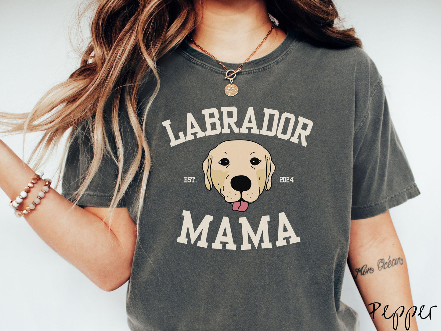 A vintage Comfort Colors t-shirt featuring bold block lettering that reads 'Labrador Mama.' At the center of the design, a playful yellow Labrador with its tongue out steals the spotlight, framed by the stylish text 'EST. 2024.'