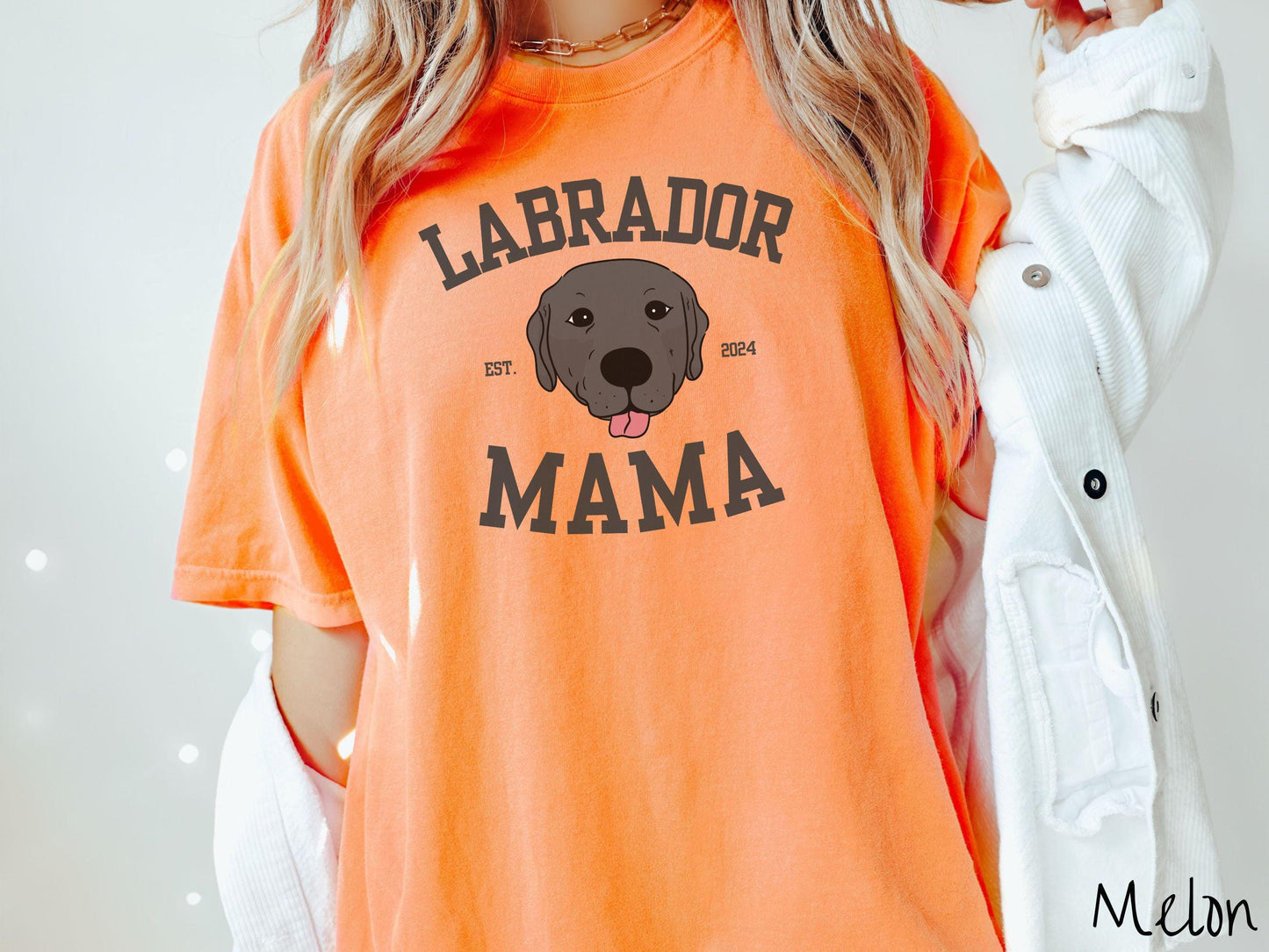 A vintage Comfort Colors t-shirt featuring bold block lettering that reads 'Labrador Mama.' At the center of the design, a playful black Labrador with its tongue out steals the spotlight, framed by the stylish text 'EST. 2024.'