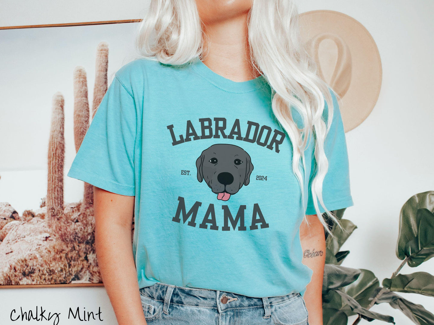 A vintage Comfort Colors t-shirt featuring bold block lettering that reads 'Labrador Mama.' At the center of the design, a playful black Labrador with its tongue out steals the spotlight, framed by the stylish text 'EST. 2024.'