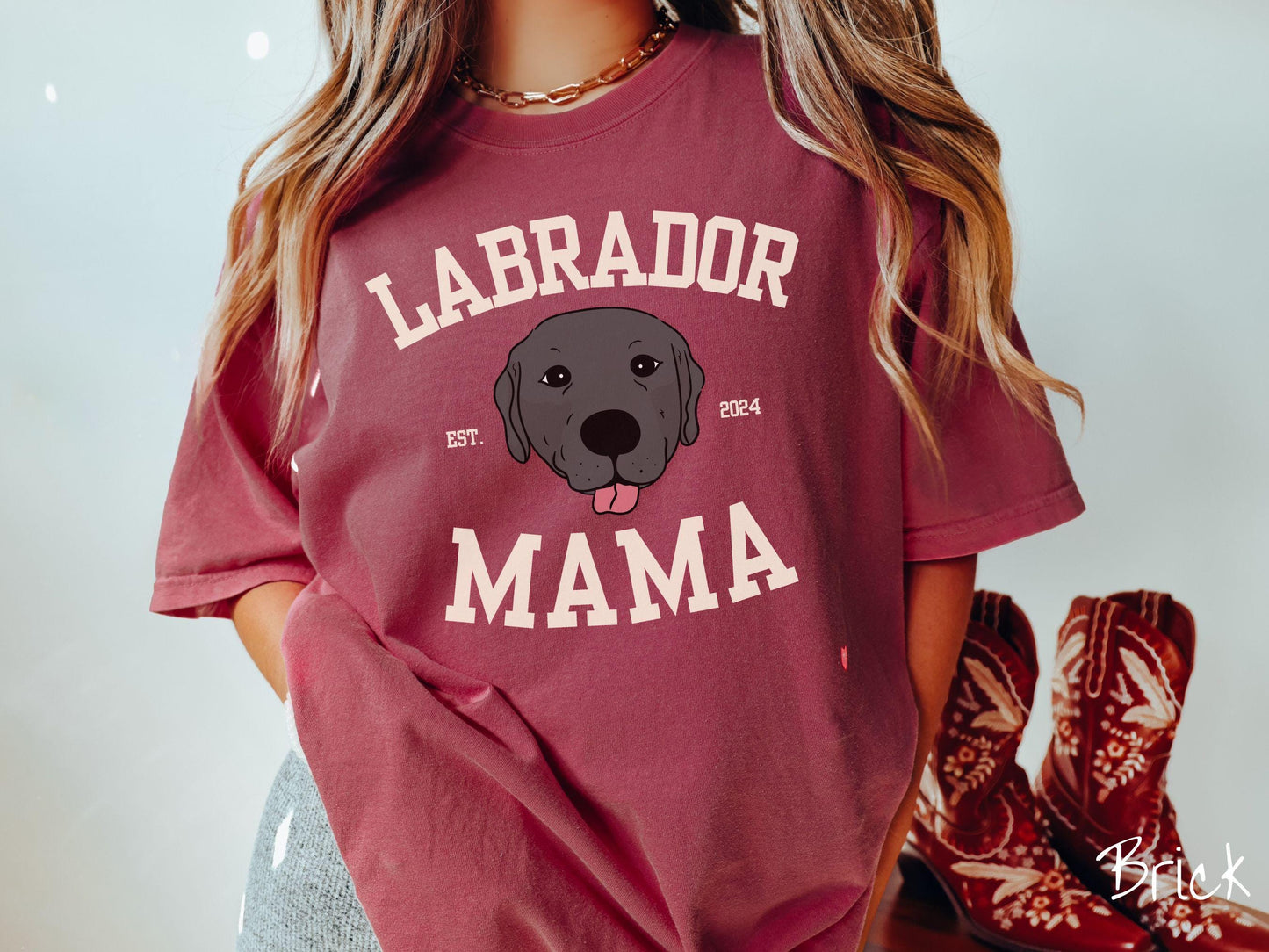 A vintage Comfort Colors t-shirt featuring bold block lettering that reads 'Labrador Mama.' At the center of the design, a playful black Labrador with its tongue out steals the spotlight, framed by the stylish text 'EST. 2024.'