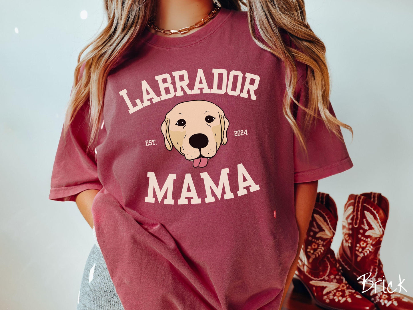A vintage Comfort Colors t-shirt featuring bold block lettering that reads 'Labrador Mama.' At the center of the design, a playful yellow Labrador with its tongue out steals the spotlight, framed by the stylish text 'EST. 2024.'