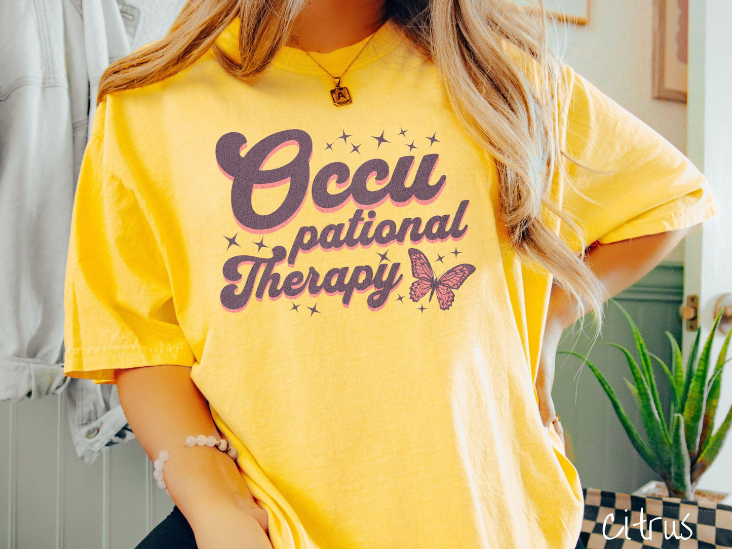 A vintage, citrus colored Comfort Colors t-shirt featuring the words Occupational Therapy across the front, this unique design showcases a stunning pink and dark purple butterfly surrounded by delicate twinkling stars.