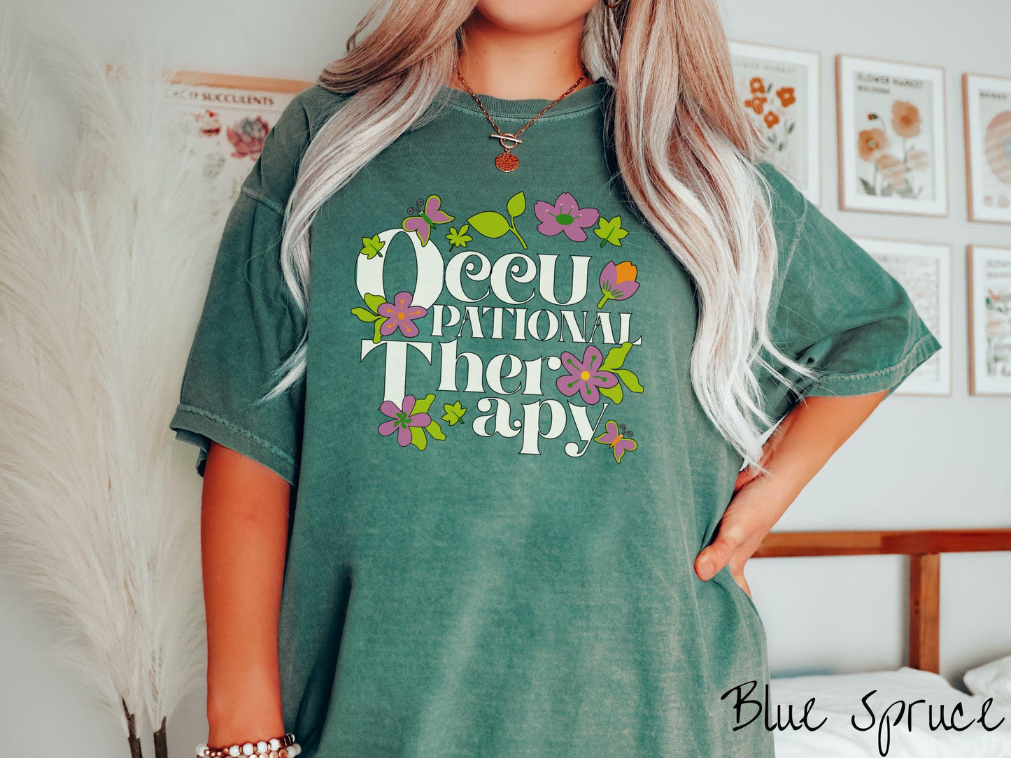 A vintage, blue spruce colored Comfort Colors t-shirt with the text Occupational Therapy and featuring green leaves, purple and orange flowers, and colorful butterflies in the background.