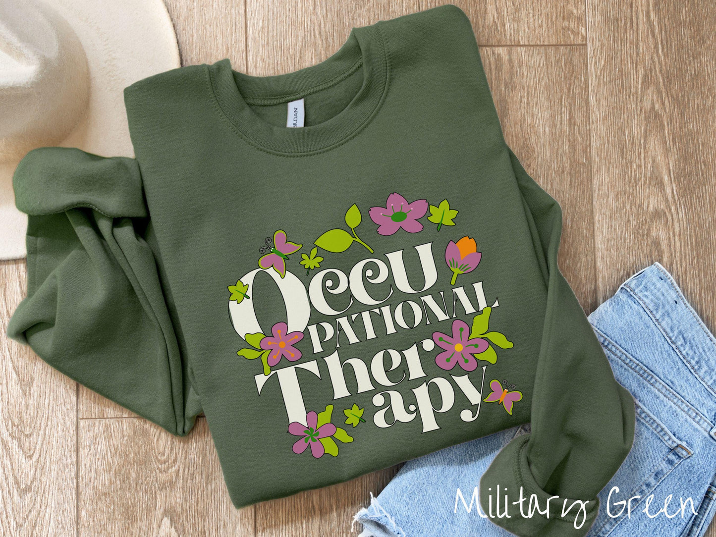 A vintage, military green colored Gildan sweatshirt with the text Occupational Therapy and featuring green leaves, purple and orange flowers, and colorful butterflies in the background.