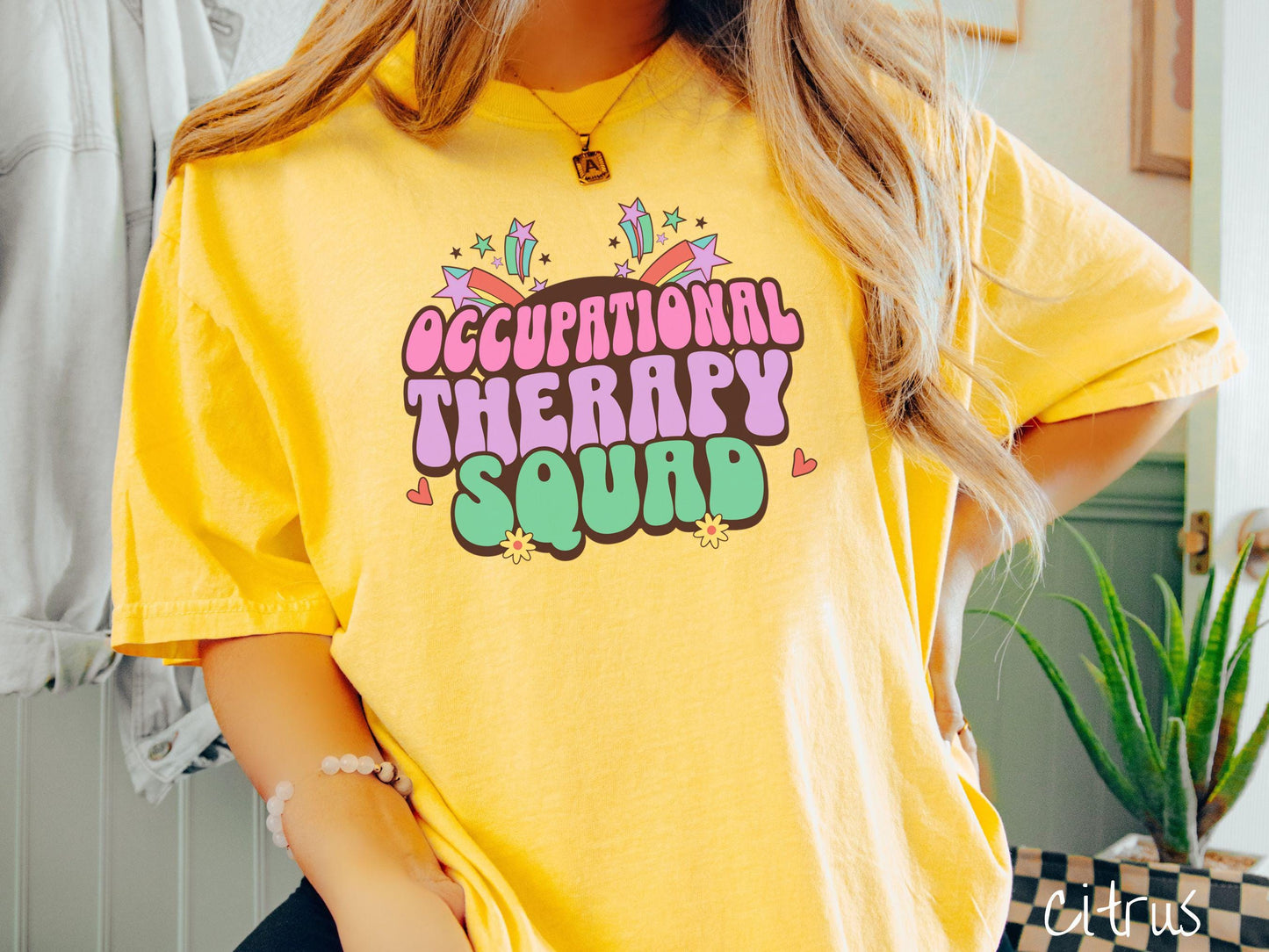 A vintage, citrus colored Comfort Colors T-shirt with the text Occupational Therapy Squad in colorful font with red hearts, sunflowers, and shooting stars mixed in.