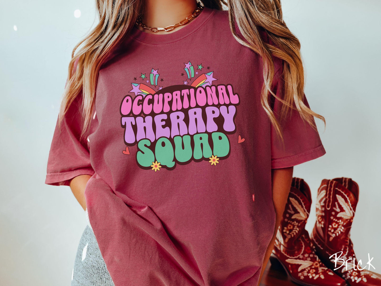 A vintage, brick colored Comfort Colors T-shirt with the text Occupational Therapy Squad in colorful font with red hearts, sunflowers, and shooting stars mixed in.