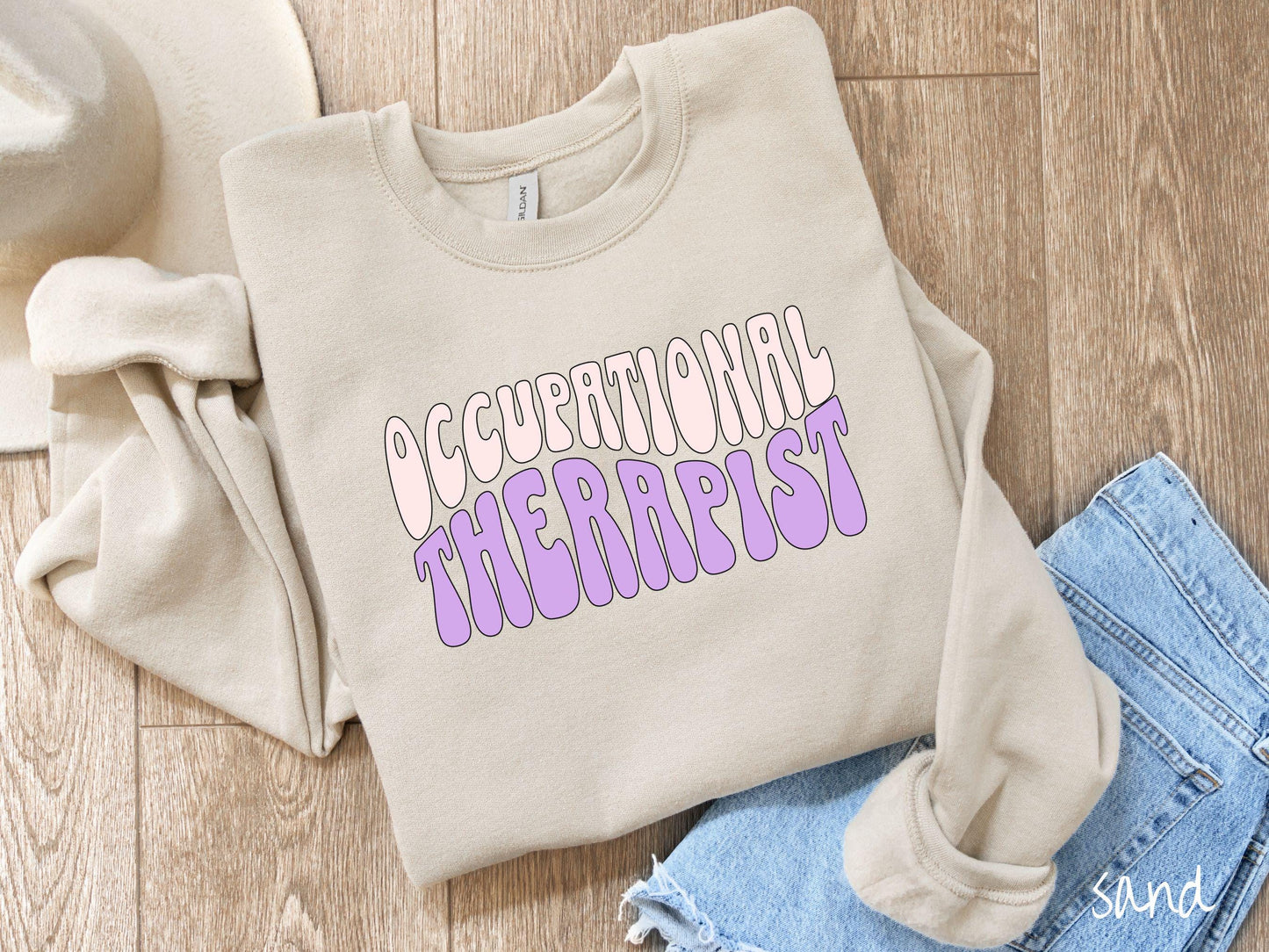 A vintage, sand colored Gildan sweatshirt featuring the text Occupational Therapist in fun wavy font. This sweater is perfect for occupational therapists looking to add a touch of personality to their casual or semi-formal outfits.