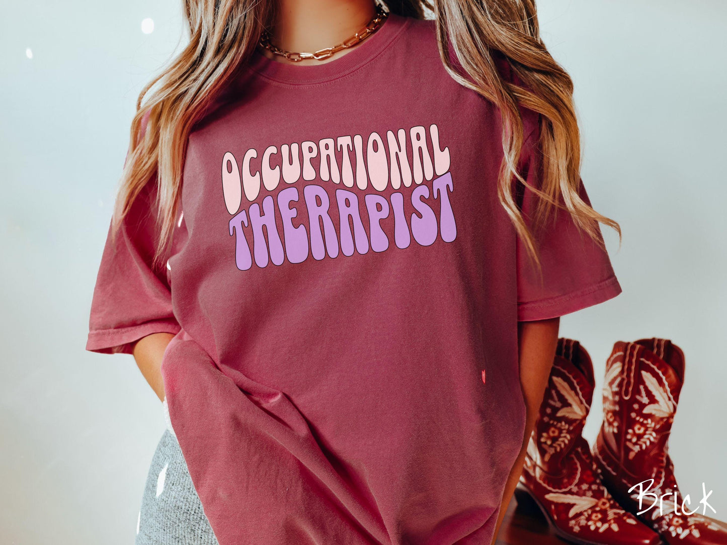 A vintage, brick colored Comfort Colors t-shirt featuring the text Occupational Therapist in fun wavy font. This sweater is perfect for occupational therapists looking to add a touch of personality to their casual or semi-formal outfits.