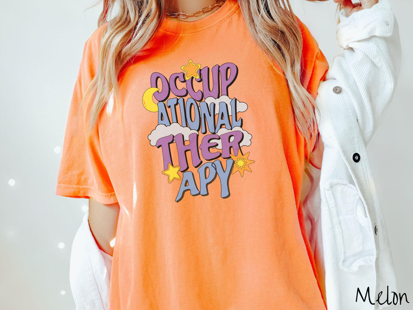 A vintage, melon colored Comfort Colors t-shirt with the text Occupational Therapy vertically with clouds, the yellow moon, and bright yellow and orange stars mixed in.
