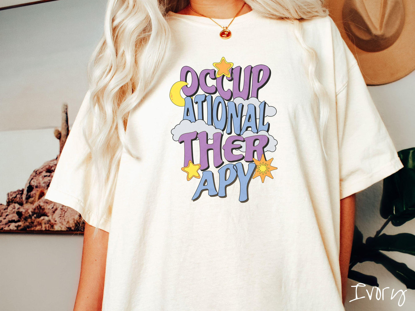 A vintage, ivory colored Comfort Colors t-shirt with the text Occupational Therapy vertically with clouds, the yellow moon, and bright yellow and orange stars mixed in.
