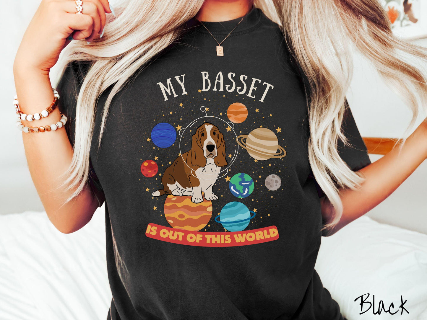 A vintage Comfort Colors t-shirt featuring the playful text 'My Basset is Out of This World'. The design showcases a basset hound sitting proudly atop Jupiter, surrounded by a vibrant solar system filled with colorful planets and twinkling stars.