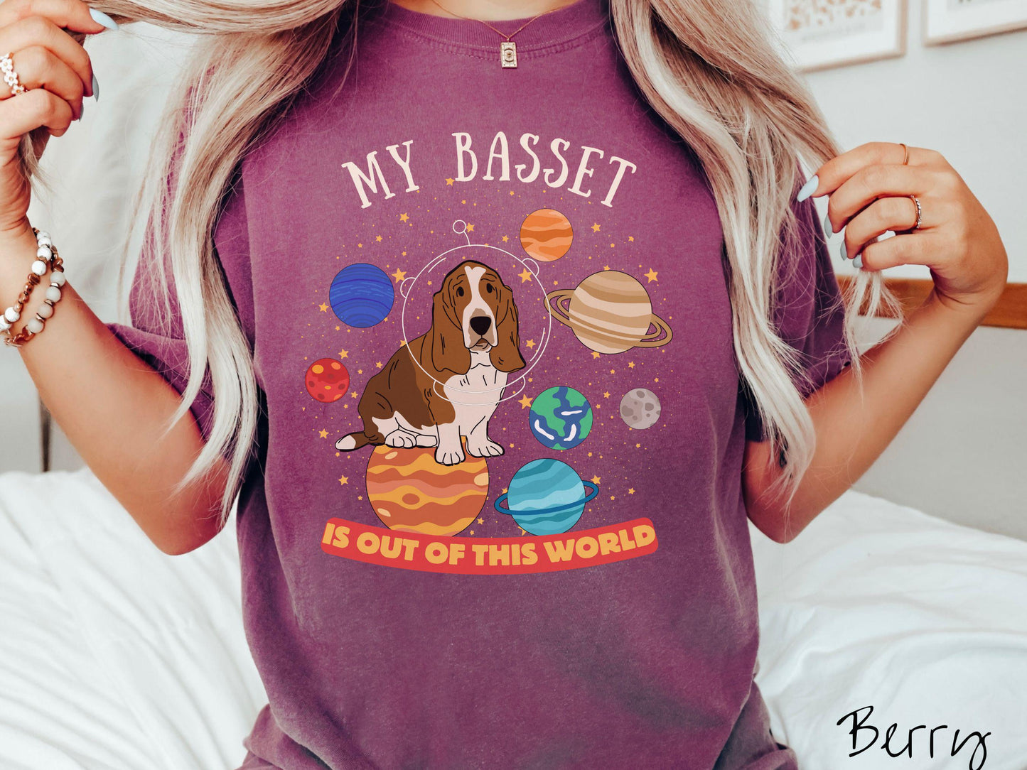 A vintage Comfort Colors t-shirt featuring the playful text 'My Basset is Out of This World'. The design showcases a basset hound sitting proudly atop Jupiter, surrounded by a vibrant solar system filled with colorful planets and twinkling stars.