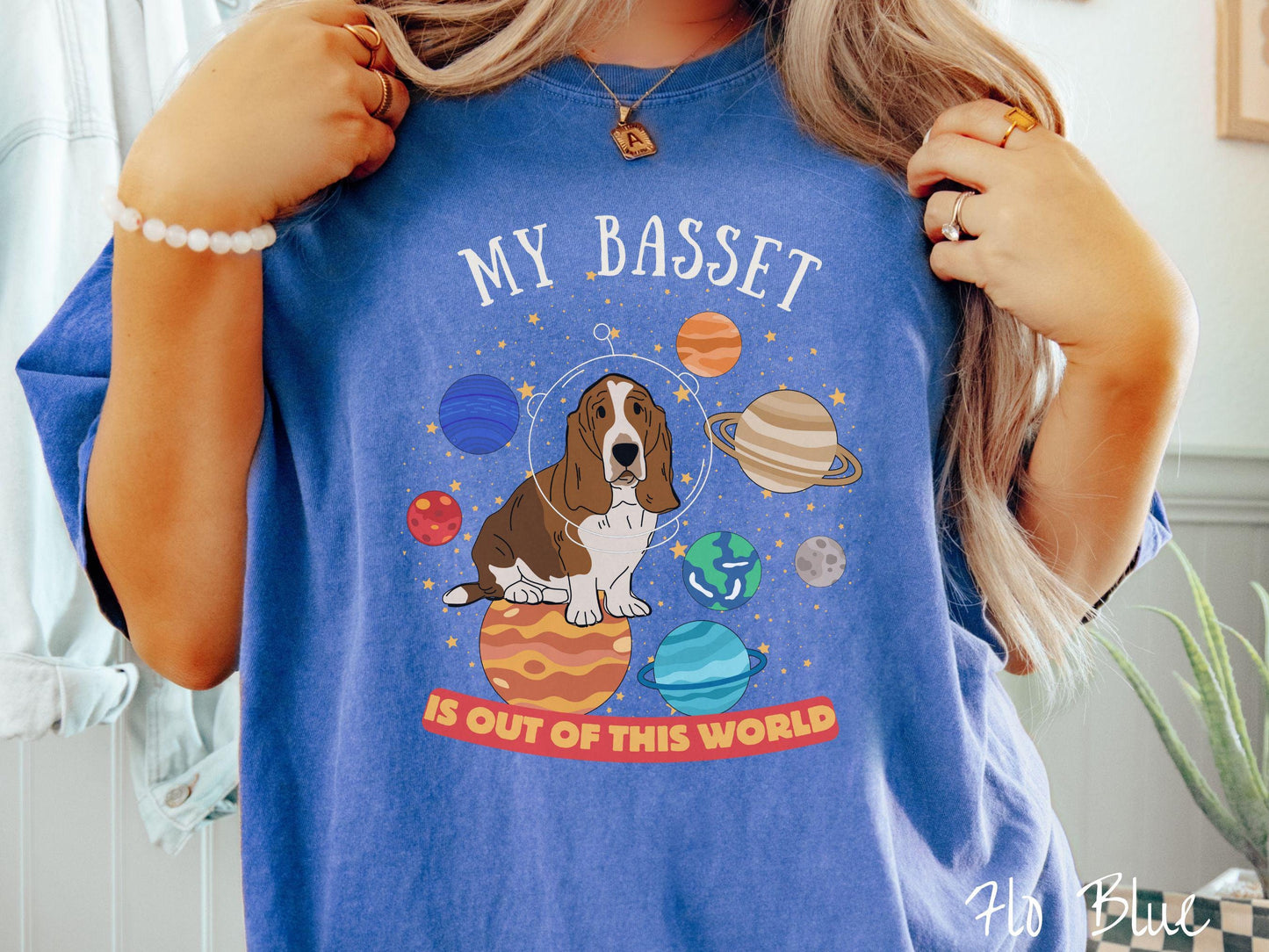 A vintage Comfort Colors t-shirt featuring the playful text 'My Basset is Out of This World'. The design showcases a basset hound sitting proudly atop Jupiter, surrounded by a vibrant solar system filled with colorful planets and twinkling stars.
