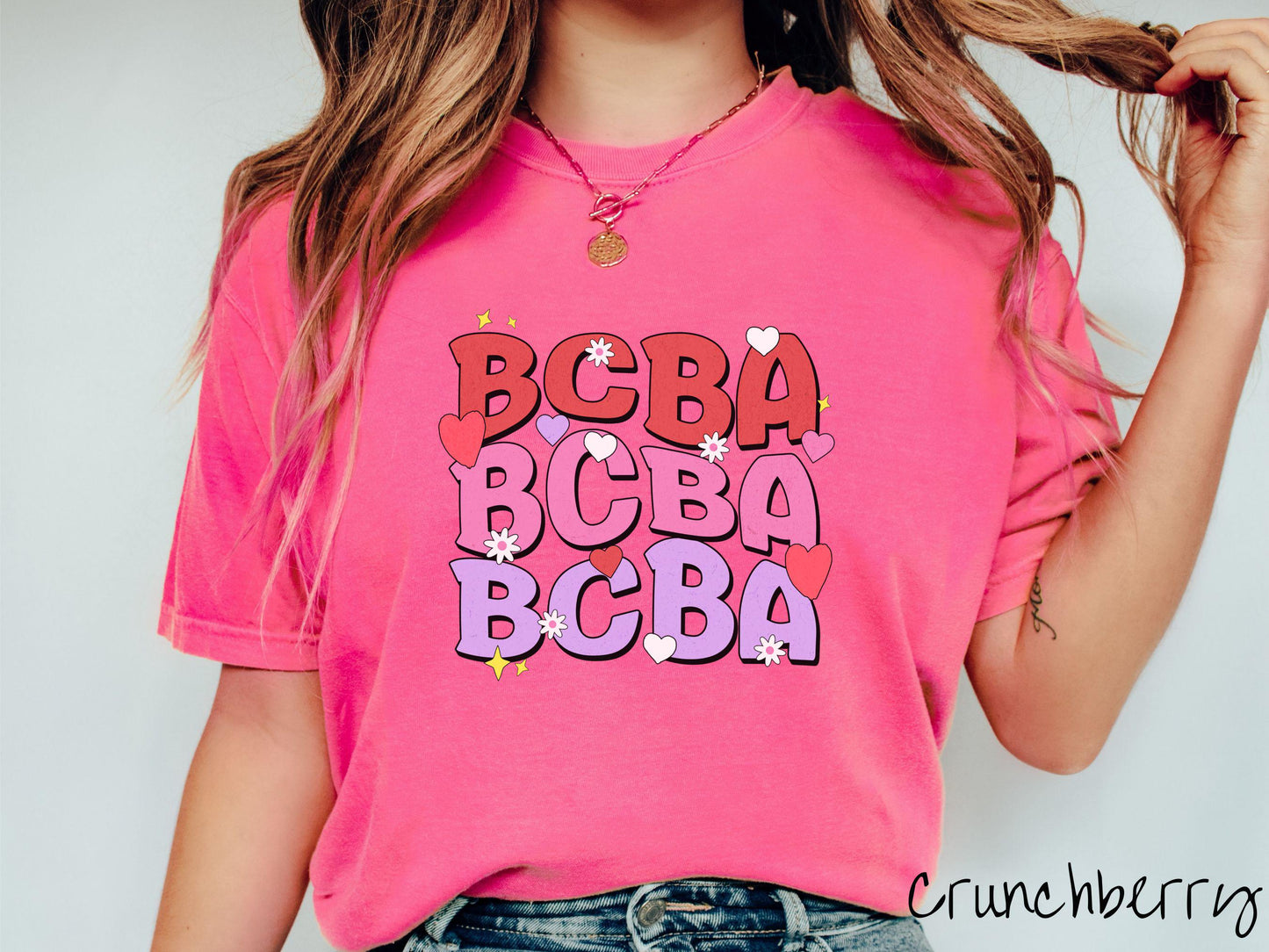 A vibrant Comfort Colors T-shirt with the text BCBA written three times vertically, accompanied by tiny hearts, stars, and flowers. Perfect for Board Certified Behavior Analysts, this tee is a great Valentine's Day gift to show appreciation and love.