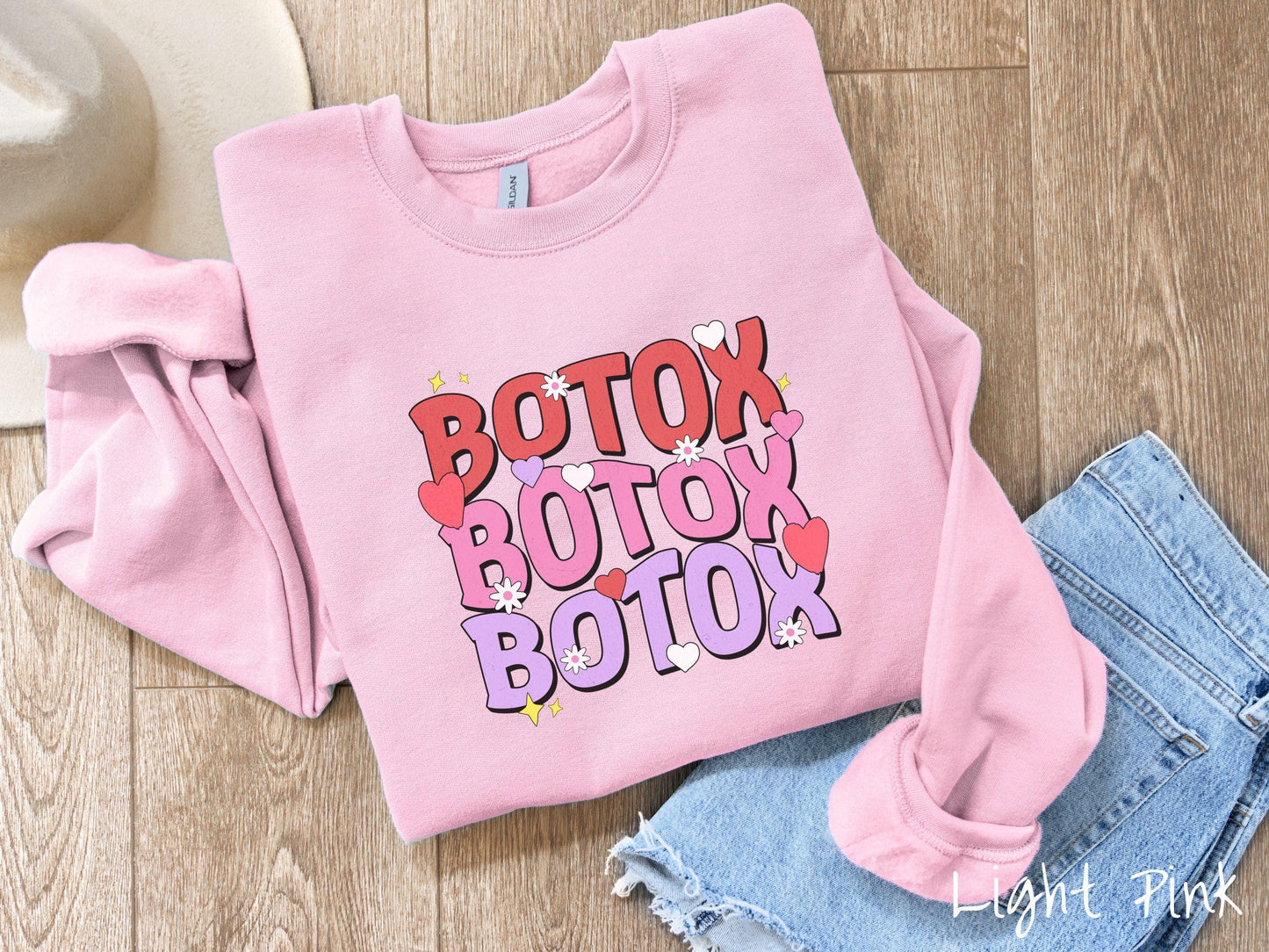 A vibrant Gildan sweatshirt with the text BOTOX written three times vertically, accompanied by tiny hearts, stars, and flowers. The perfect gift for friends who are into cosmetic botox nursing.
