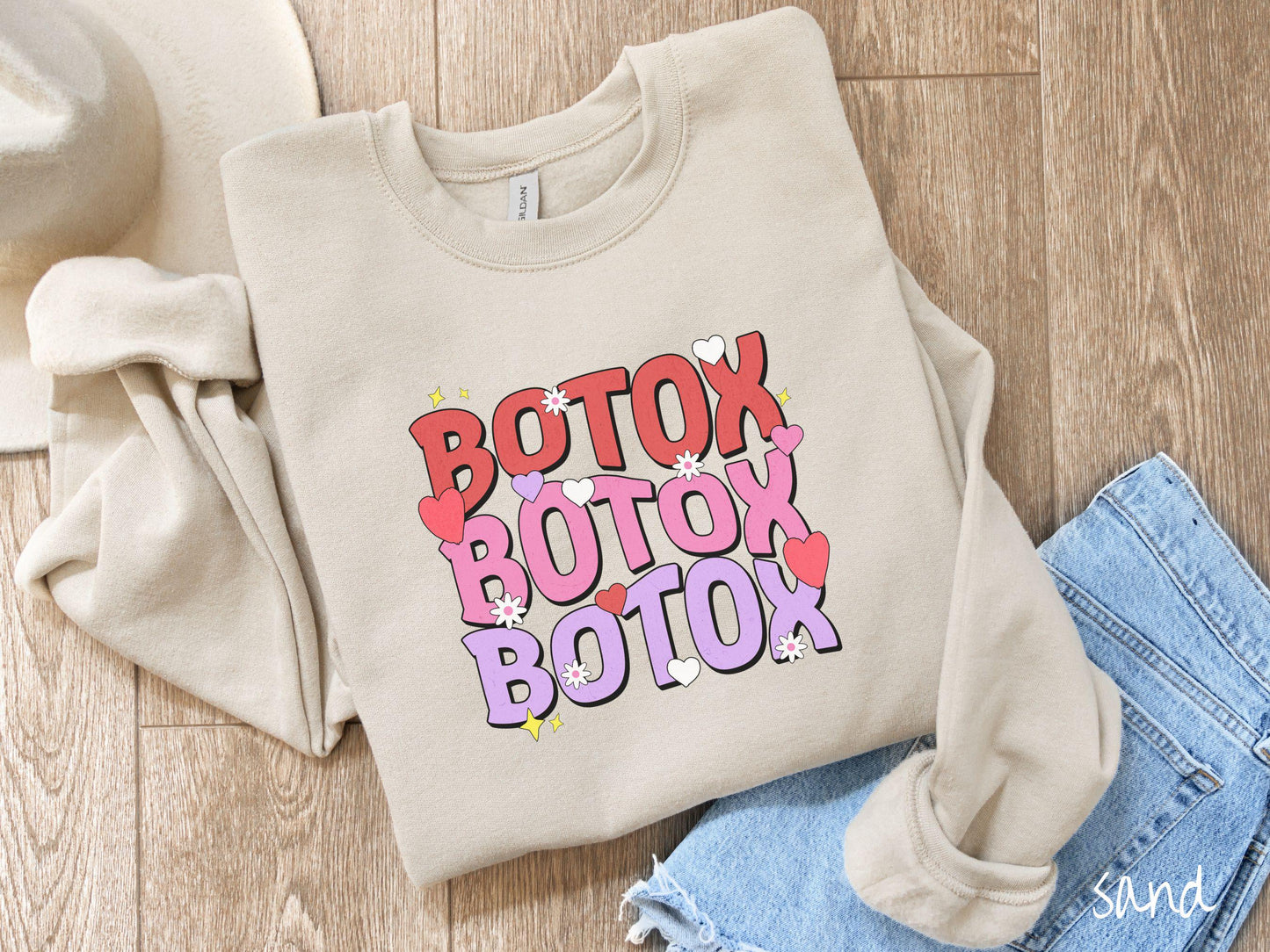 A vibrant Gildan sweatshirt with the text BOTOX written three times vertically, accompanied by tiny hearts, stars, and flowers. The perfect gift for friends who are into cosmetic botox nursing.
