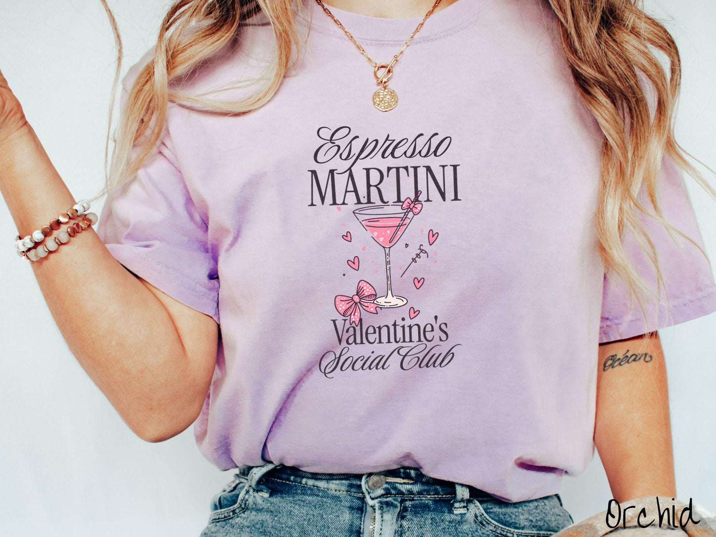 A stylish Comfort Colors T-shirt featuring the phrase "Espresso Martini" above a martini glass filled with pink martini a pink bow-topped toothpick. The words "Valentine's Social Club" appear below, with pink bows and hearts throughout the design.