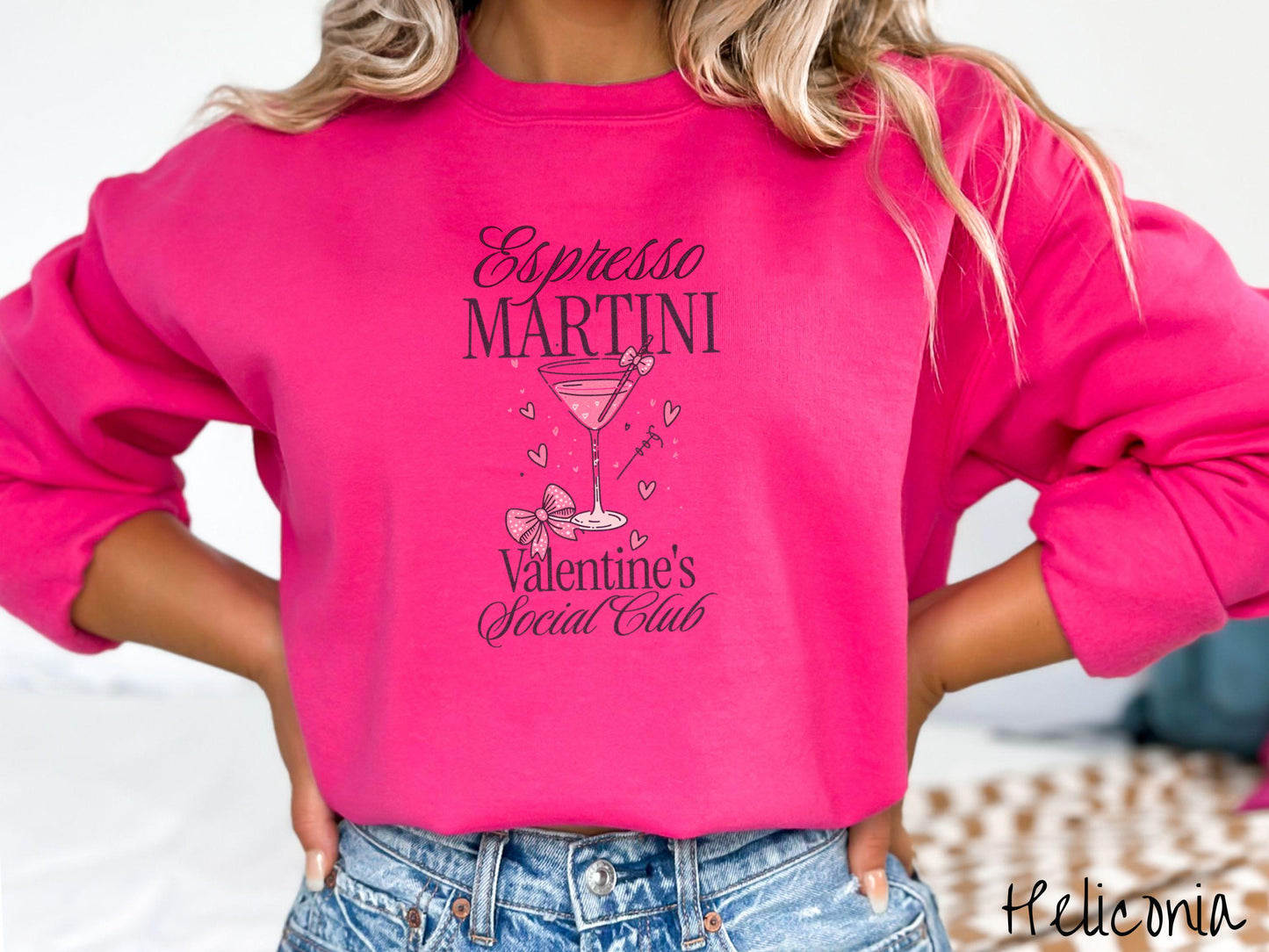 A stylish Gildan sweatshirt featuring the phrase "Espresso Martini" above a martini glass filled with pink martini and a pink bow-topped toothpick. The words "Valentine's Social Club" appear below with pink bows and hearts throughout the design.