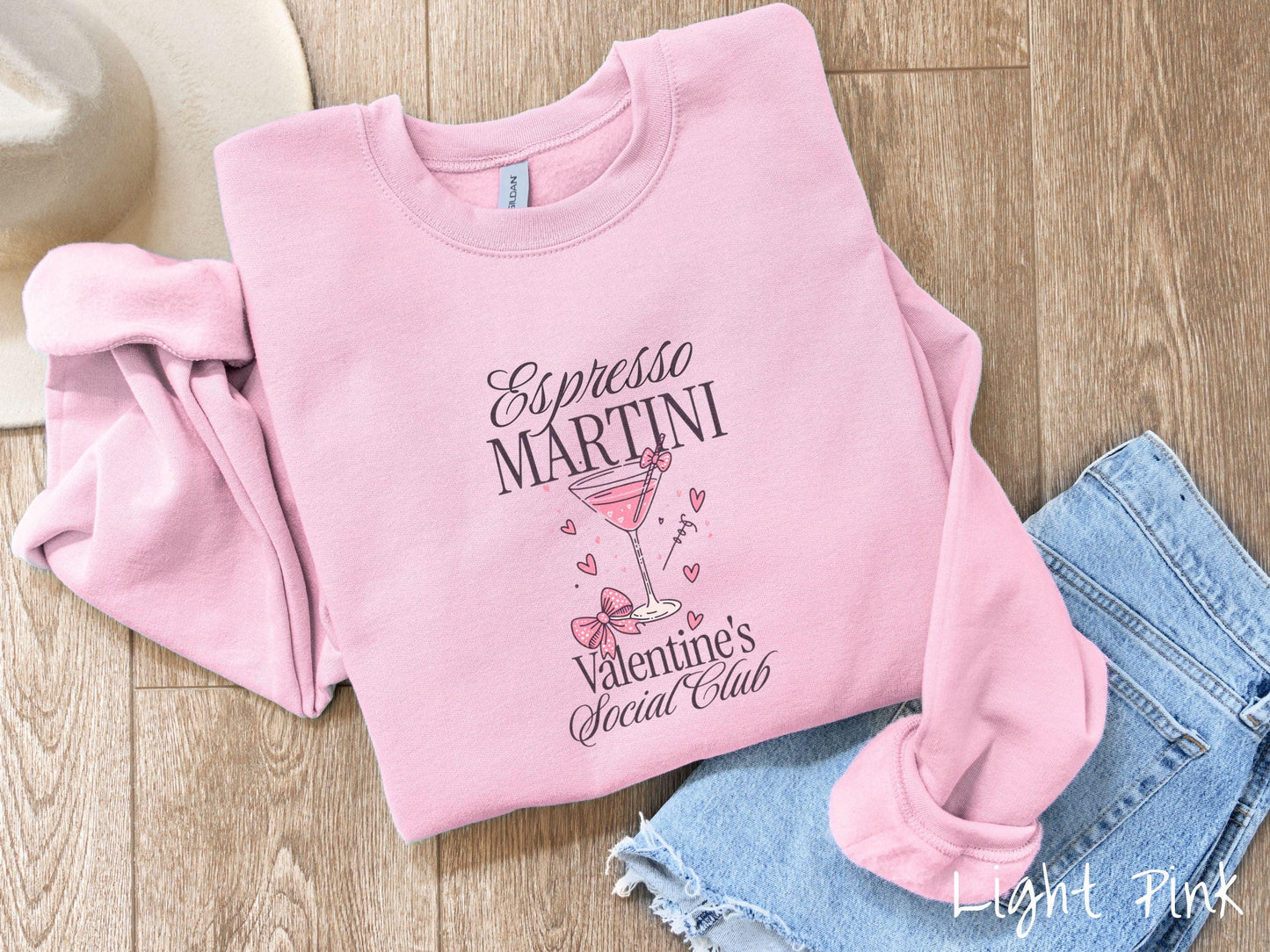 A stylish Gildan sweatshirt featuring the phrase "Espresso Martini" above a martini glass filled with pink martini and a pink bow-topped toothpick. The words "Valentine's Social Club" appear below with pink bows and hearts throughout the design.