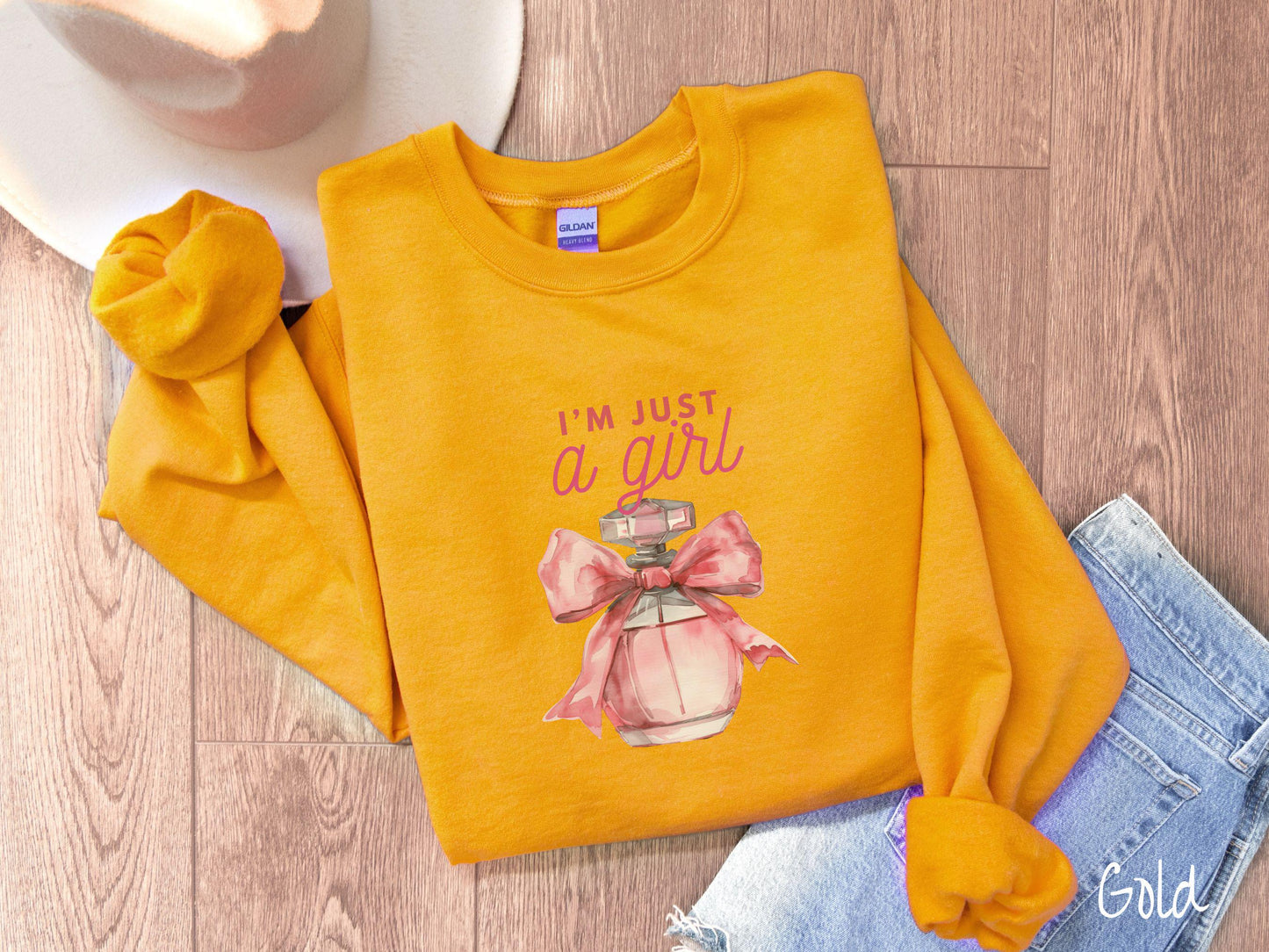 A cozy Gildan sweatshirt featuring the phrase "I'm Just a Girl" in pink font above a bottle of pink perfume tied with a pink bow. Perfect for those colder months, this sweatshirt provides warmth and comfort with its classic fit and crew neckline.